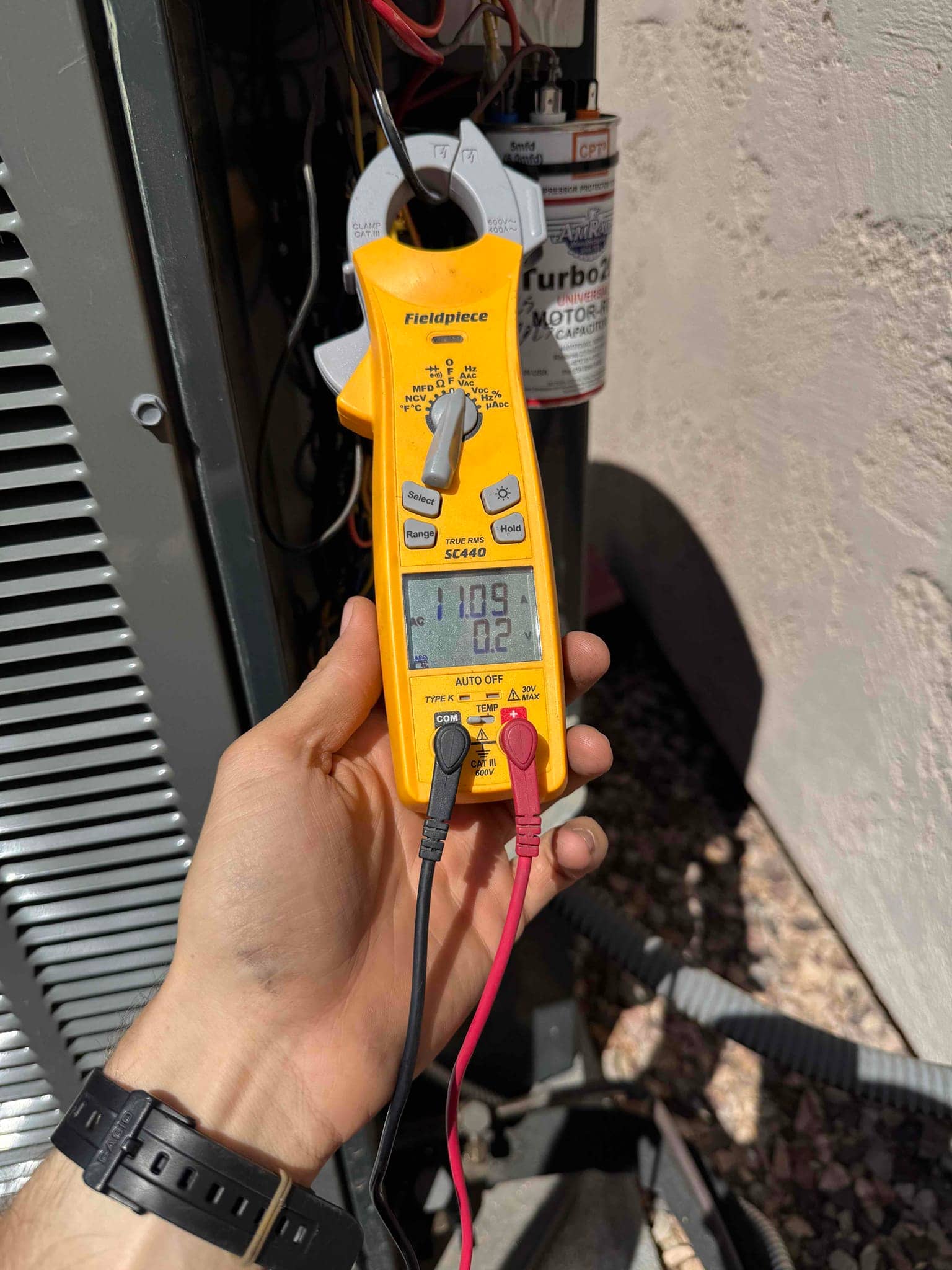 Clamp meter shows 10.92 A on the compressor common lead while testing near the outdoor condenser and run capacitor.
