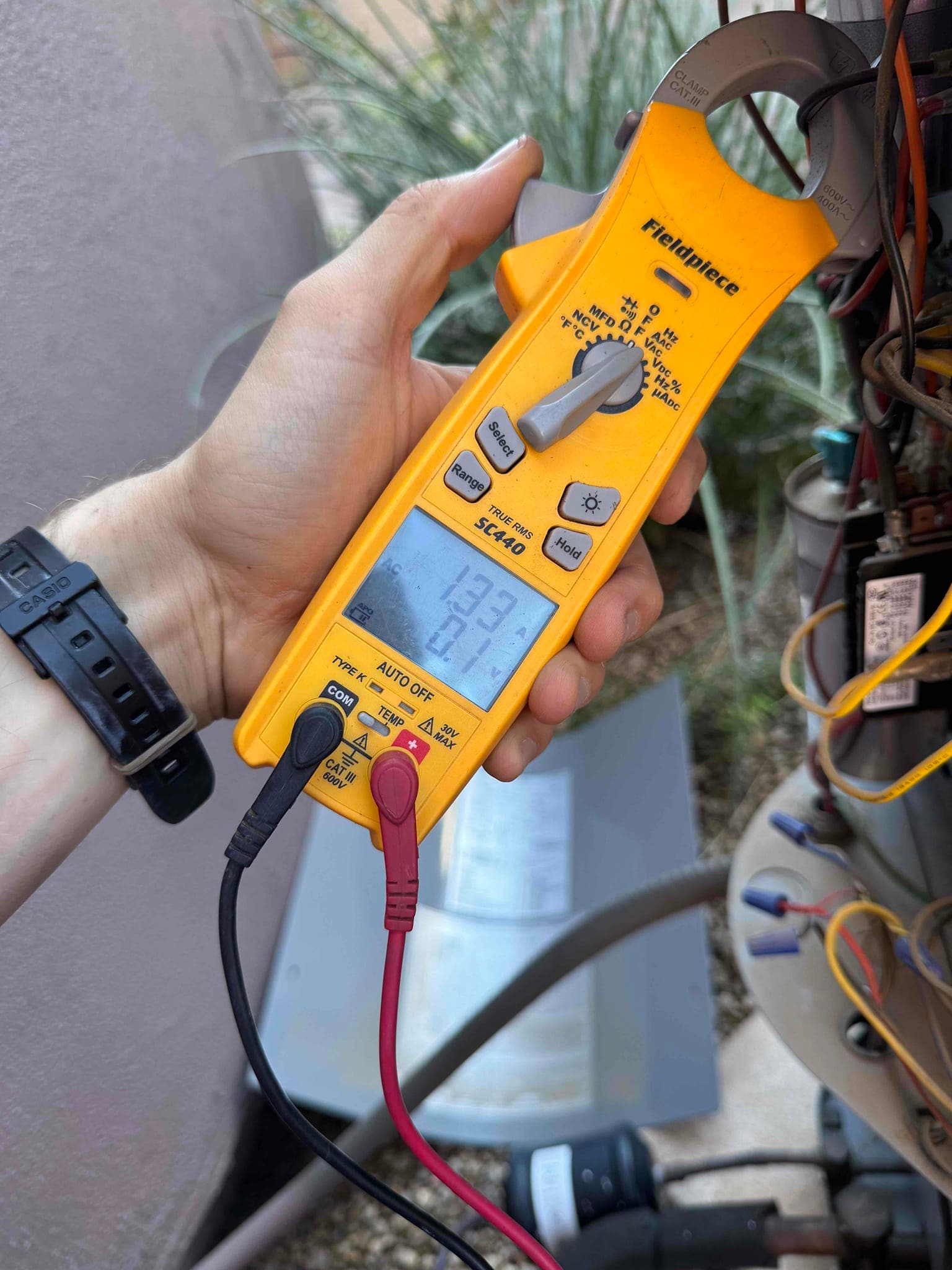 Clamp meter shows 13.91 A on a clamped conductor inside the outdoor unit wiring compartment during operation.