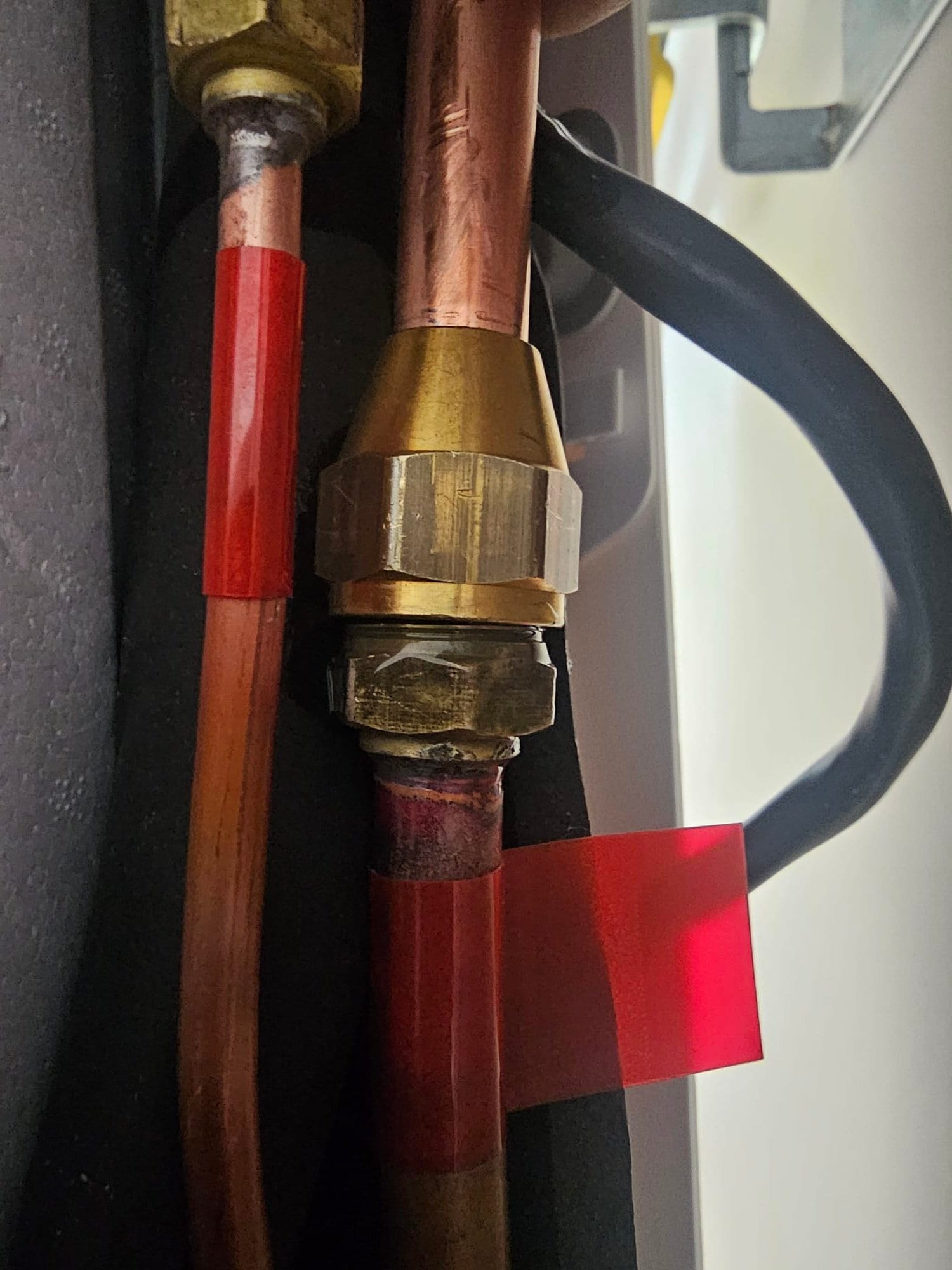 Close-up of brazed copper refrigerant lines with flare fittings and insulation during mini-split installation.