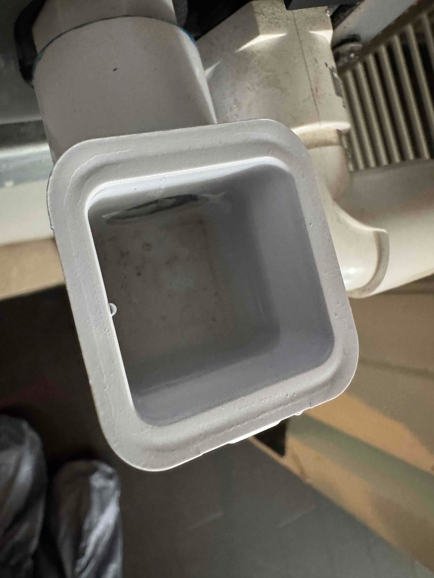 Close-up of a cleaned PVC condensate drain outlet at the air handler, showing clear, unobstructed opening.