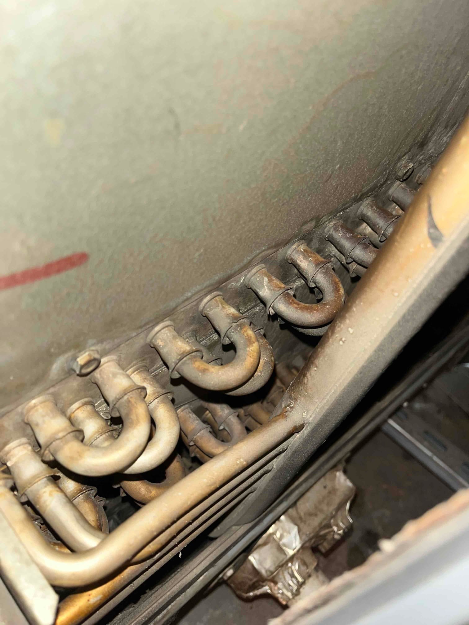 Close-up of evaporator coil tubing and U-bends inside an air handler, showing dust buildup and surface oxidation on copper lines.