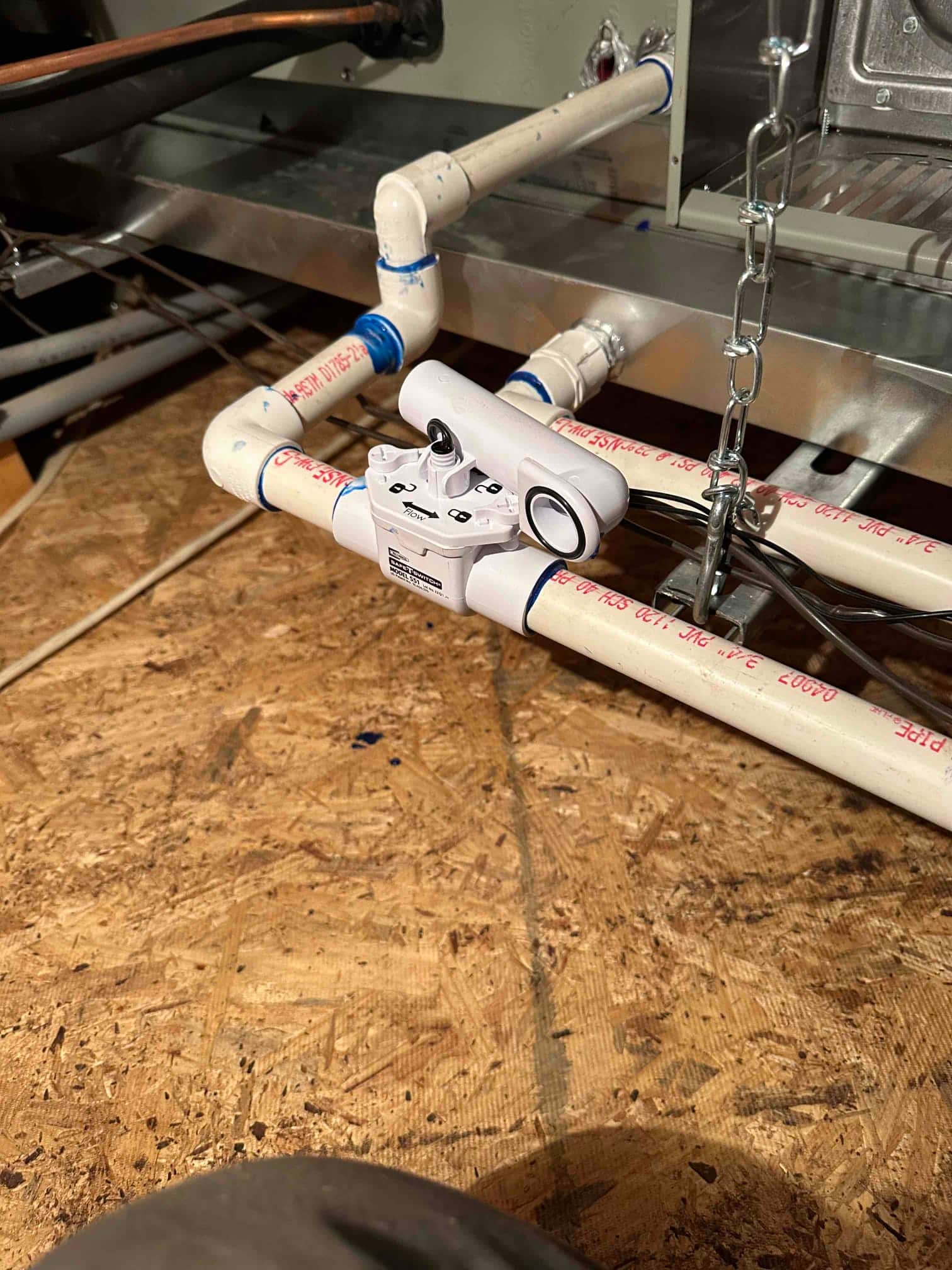 Condensate drain assembly under the air handler with cleanout, float safety switch, and glued PVC fittings.