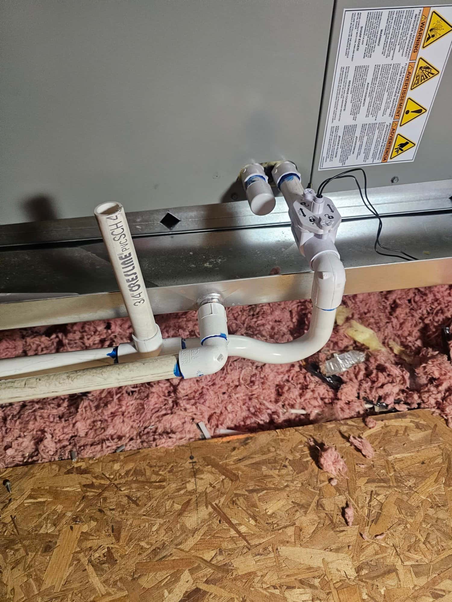 Condensate drain assembly with cleanout and float switch wired to the air handler, set above attic insulation on a platform.