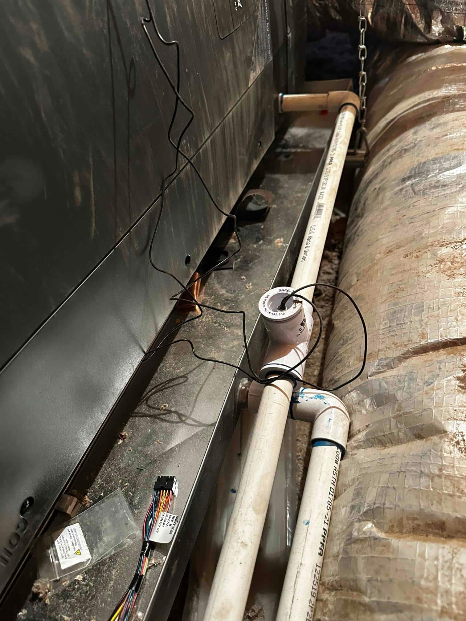 Condensate drain assembly with PVC piping and cleanout installed beside the air handler in the attic.