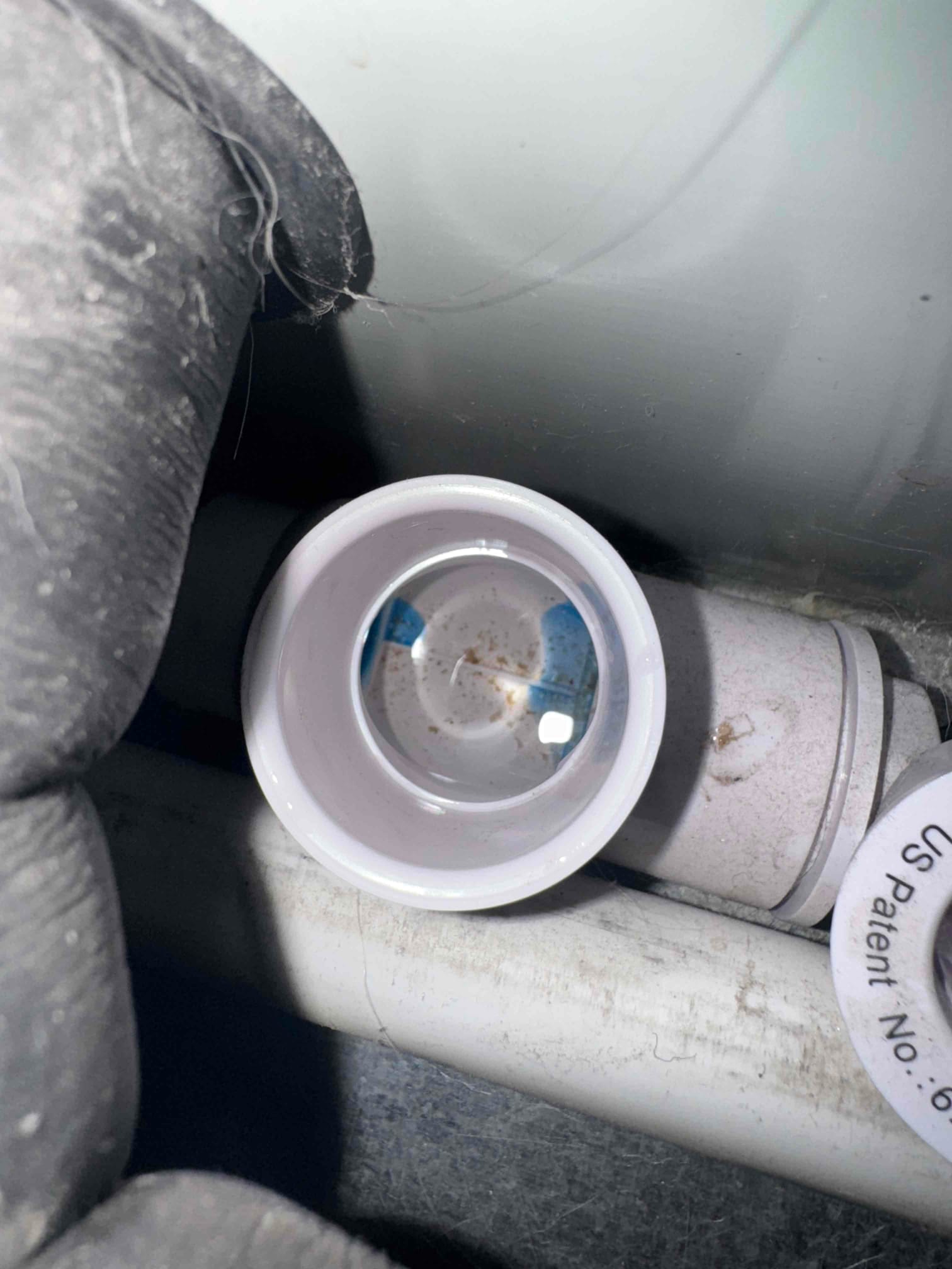 Condensate drain cleanout with water and debris visible inside PVC fitting near air handler piping.