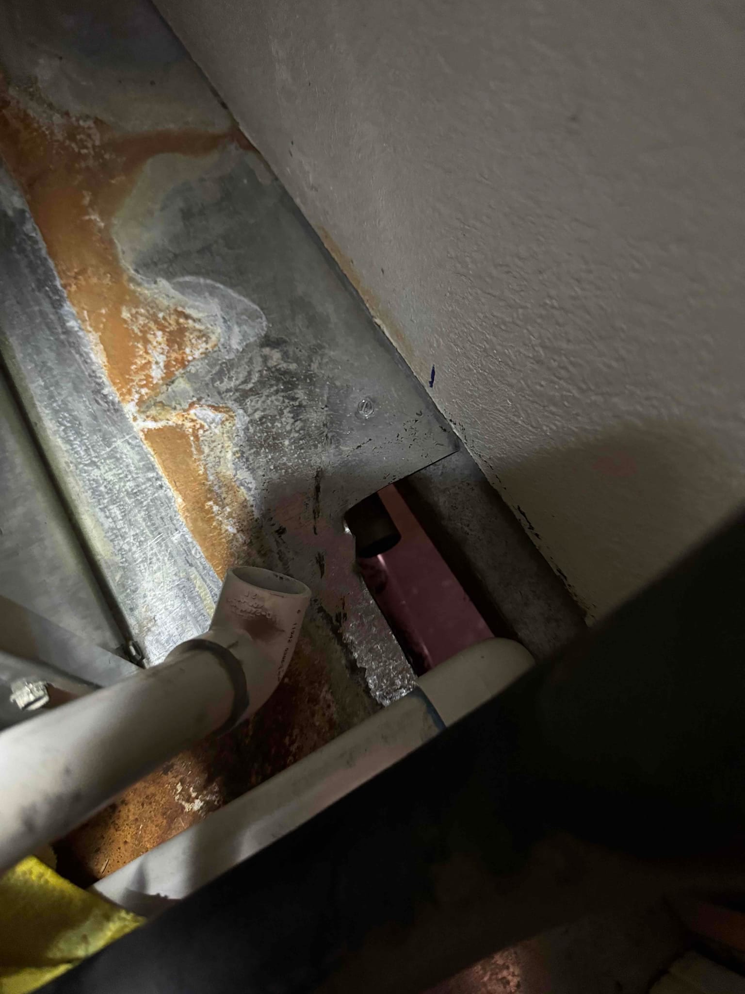 Condensate drain line and pan area inside the air handler, showing rust stains and moisture along the metal surface.