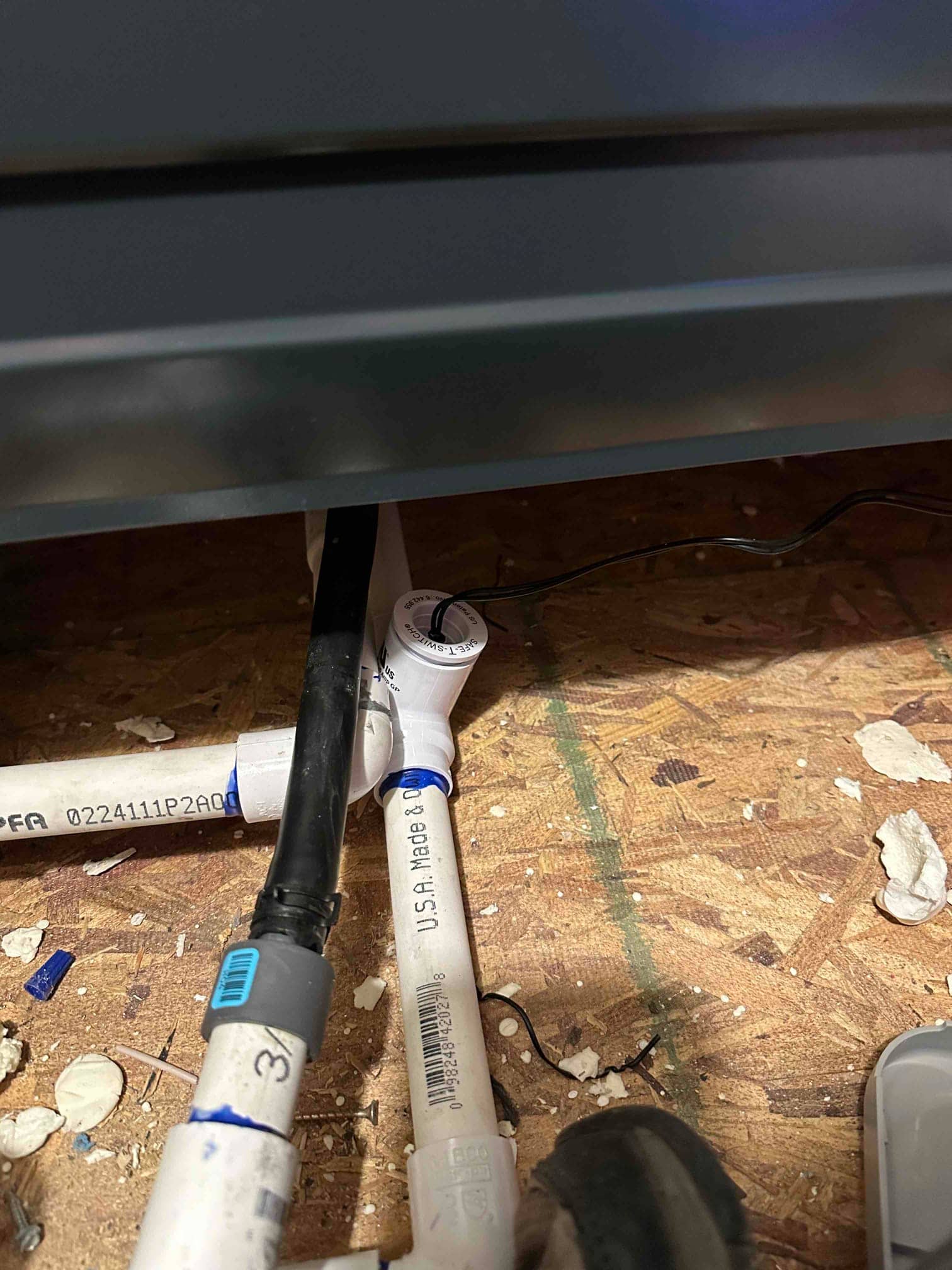 Condensate drain piping assembled beneath the indoor unit, with glued PVC fittings and a flexible drain connection visible on the floor.