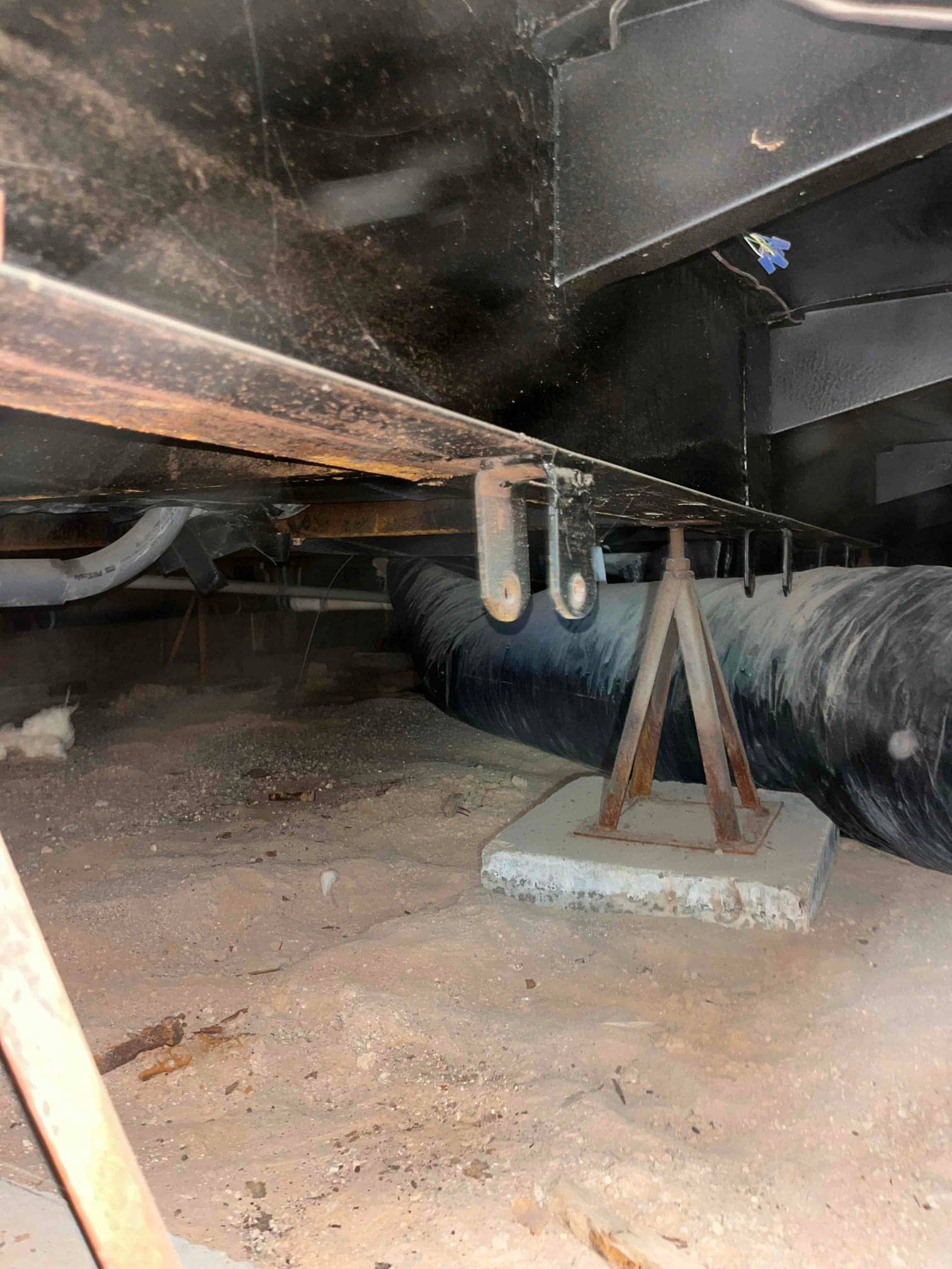 Crawlspace view shows flexible insulated duct and support stand beneath equipment platform with visible dust and debris.