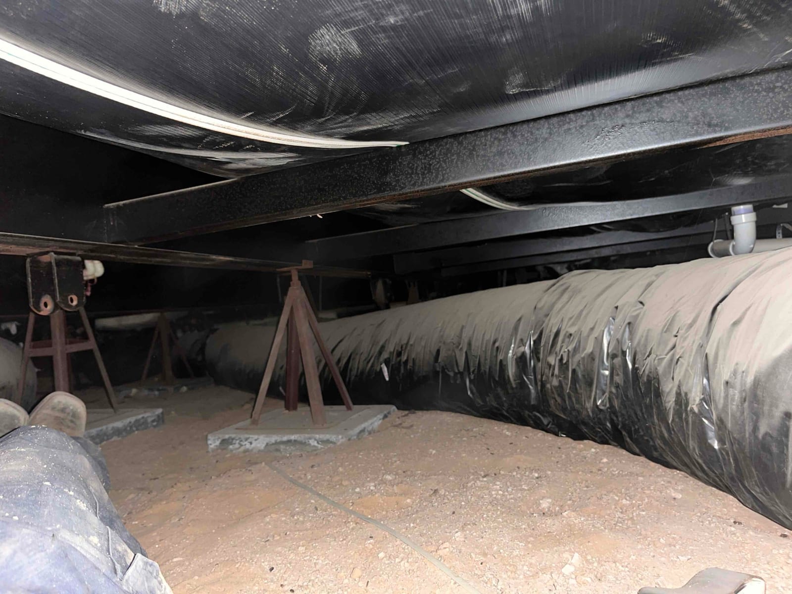 Crawlspace view shows insulated flexible ductwork on stands and support piers beneath the structure, with exposed soil floor.