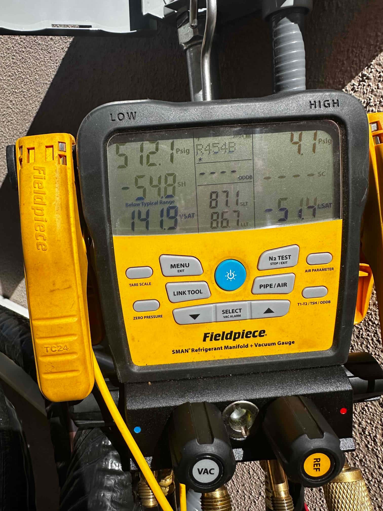 Digital manifold displays operating refrigerant pressures with R-454B selected, showing distinct low and high side readings during system commissioning.