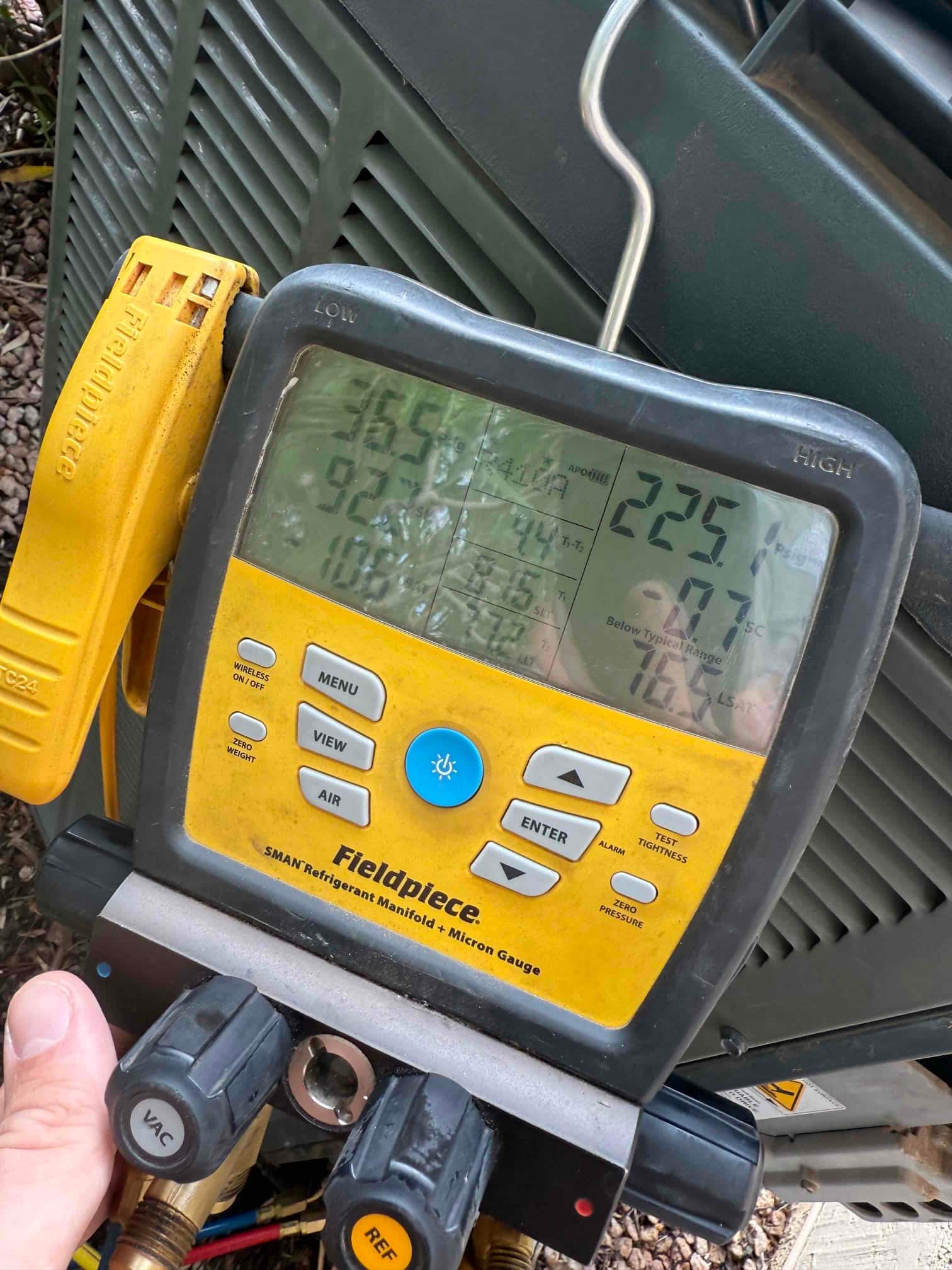 Digital manifold gauge connected to an outdoor condenser shows 225 psi on the high side during refrigerant charging.