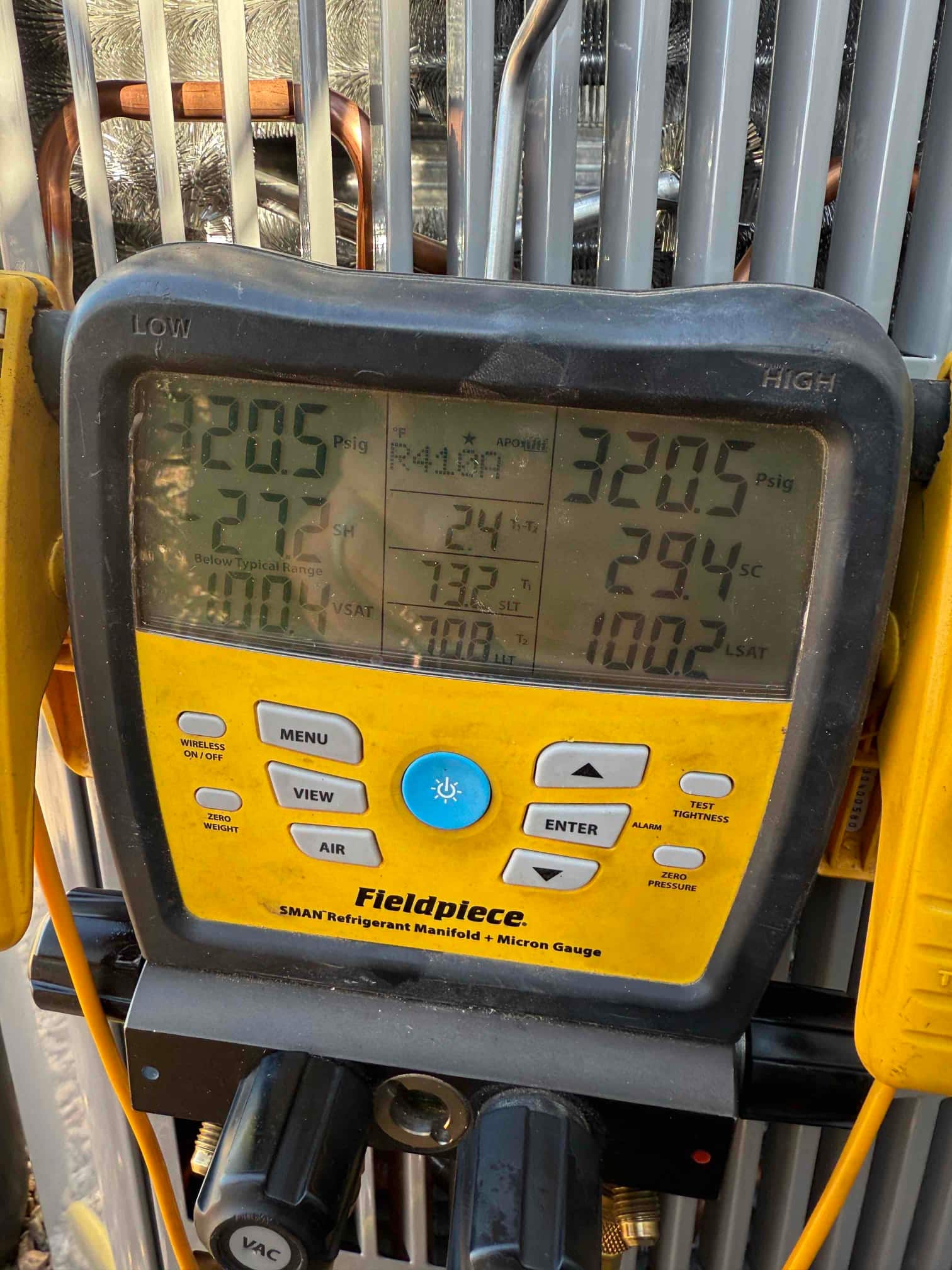 Digital manifold shows operating pressures on a running air conditioning system during refrigerant commissioning at the outdoor unit.
