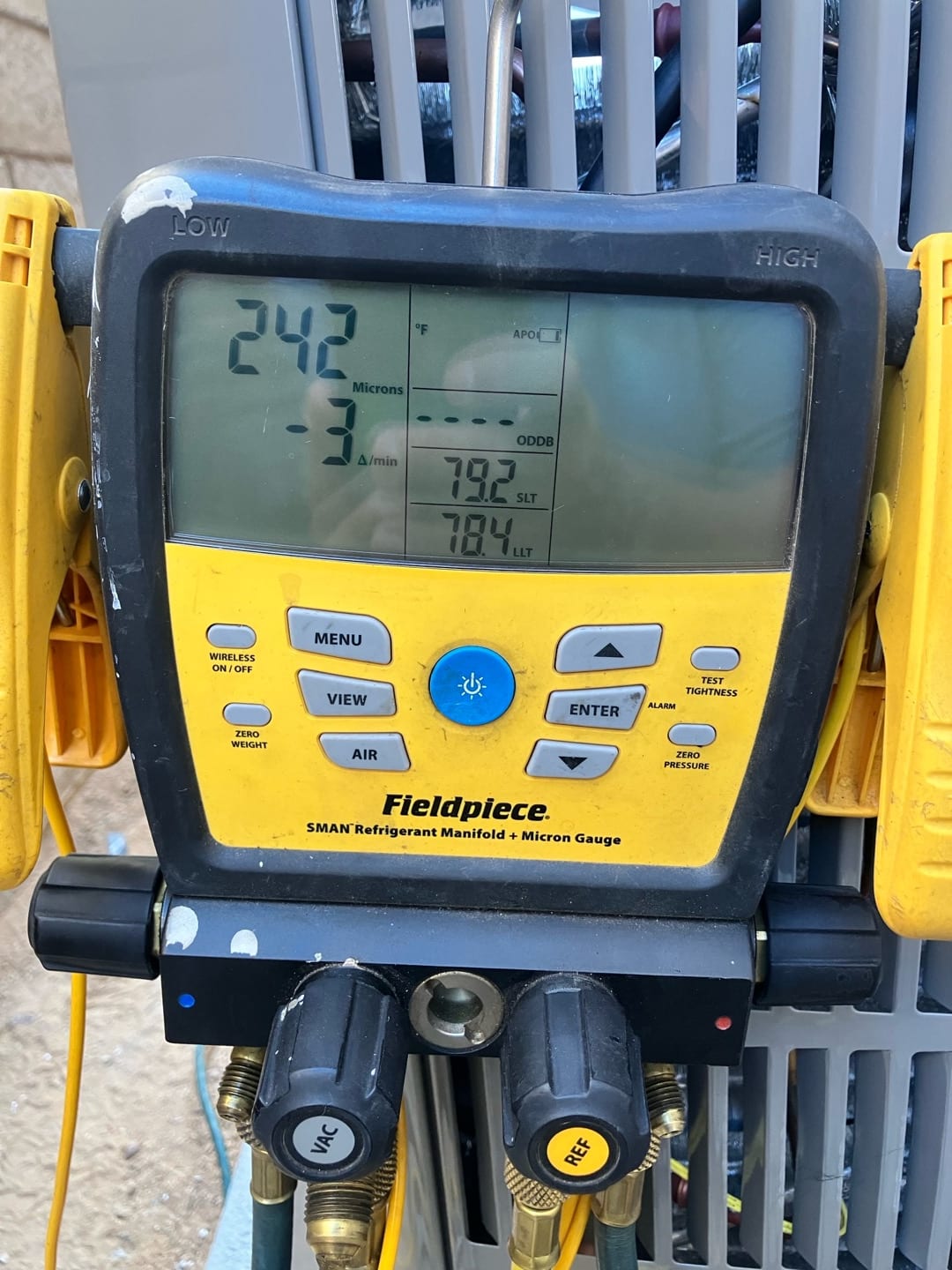 Digital micron gauge shows 242 microns with a decreasing rate, documenting deep vacuum during system evacuation before refrigerant charging.