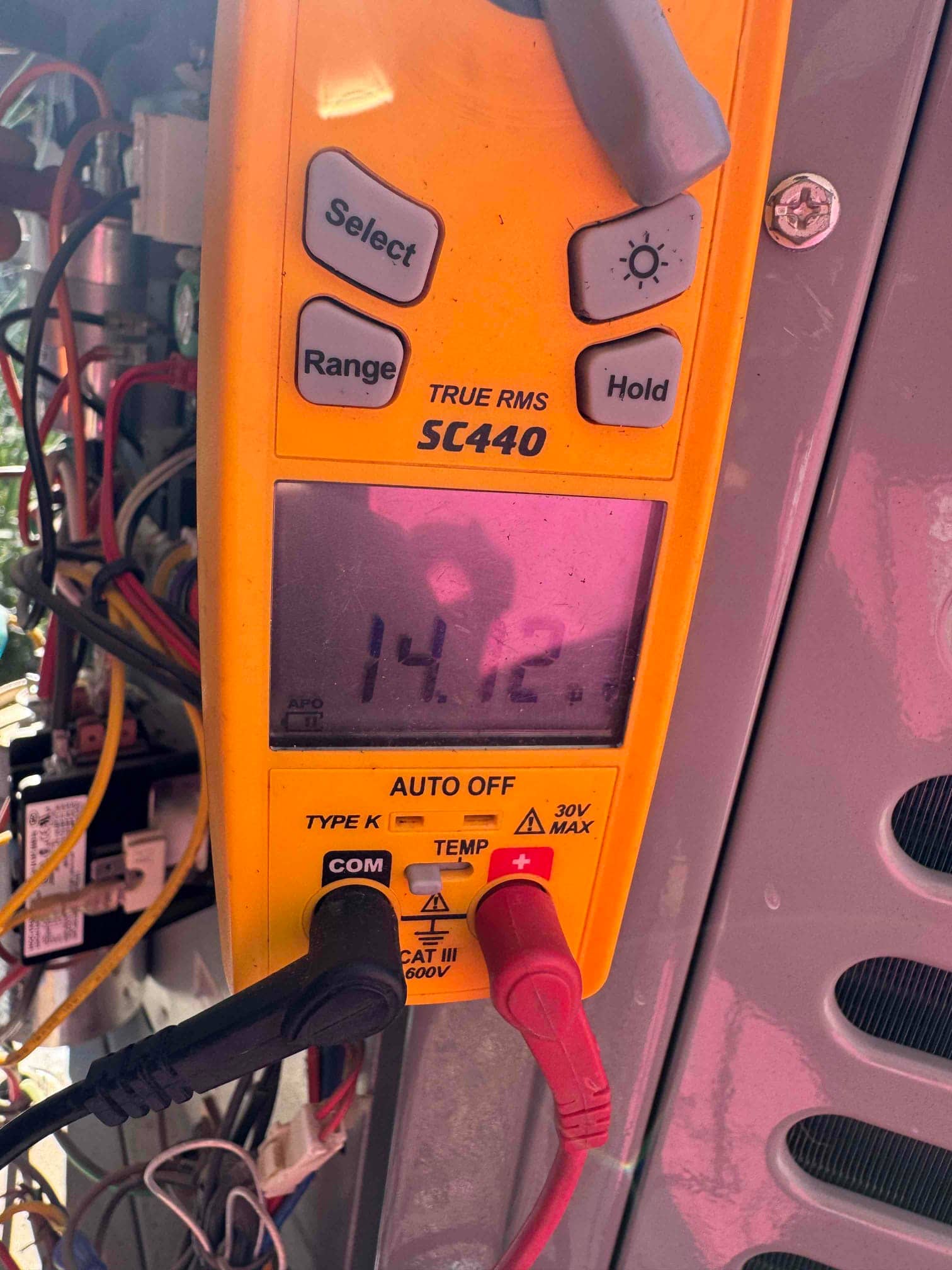 Digital multimeter connected at the outdoor unit control panel shows 14.12 V on the display during testing.