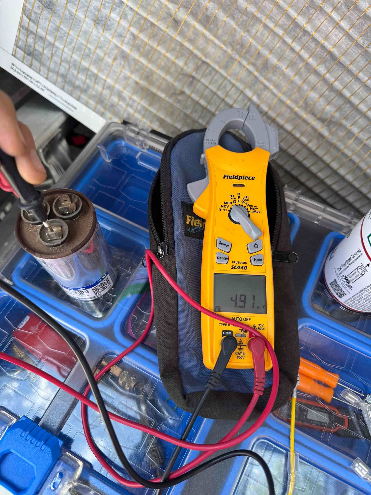 Digital multimeter measures 49.1 μF on the removed run capacitor with test leads connected to its terminals.