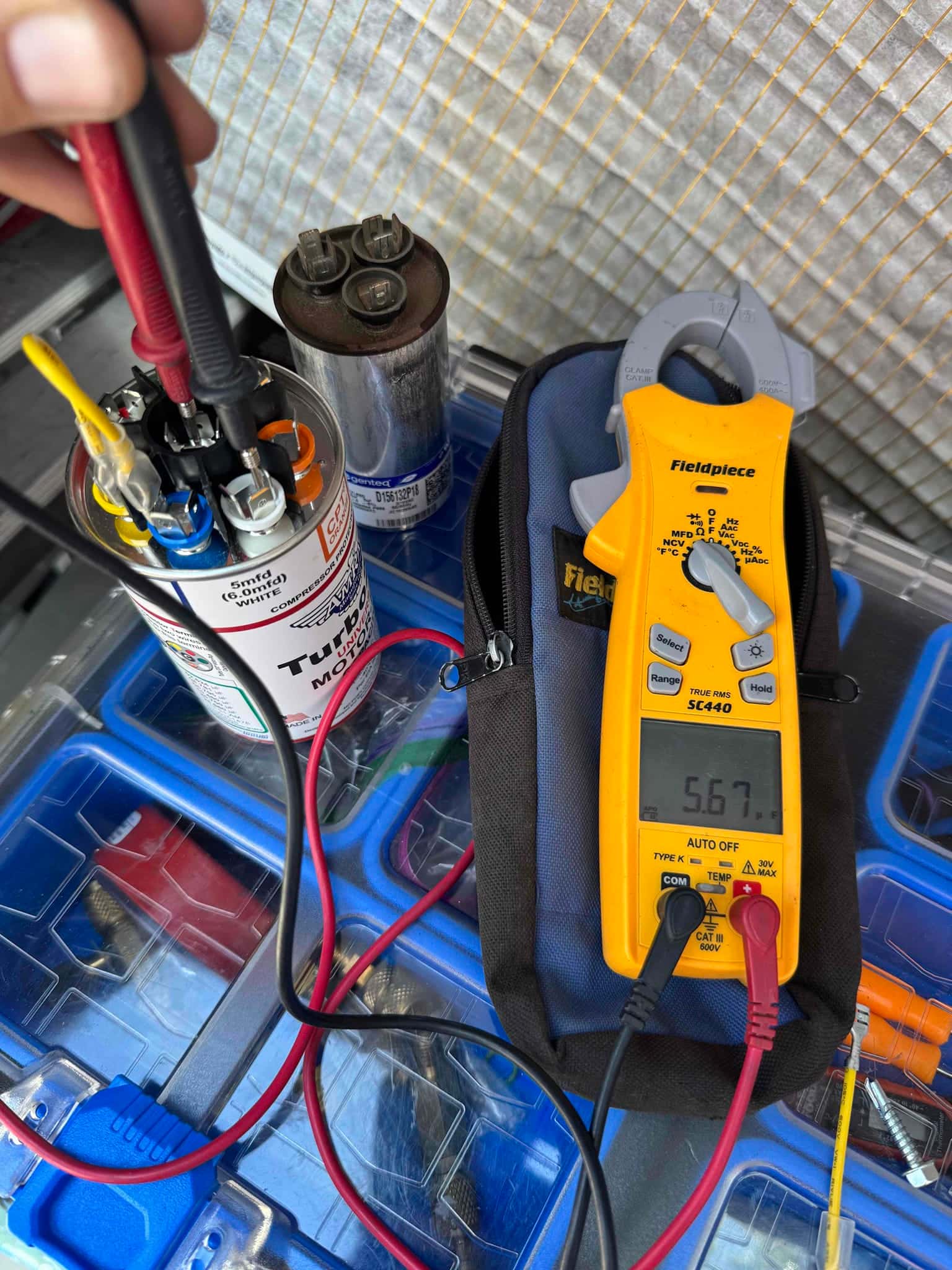 Digital multimeter measures 56.7 μF on the dual-run capacitor terminals during testing, with test leads connected to the capacitor.