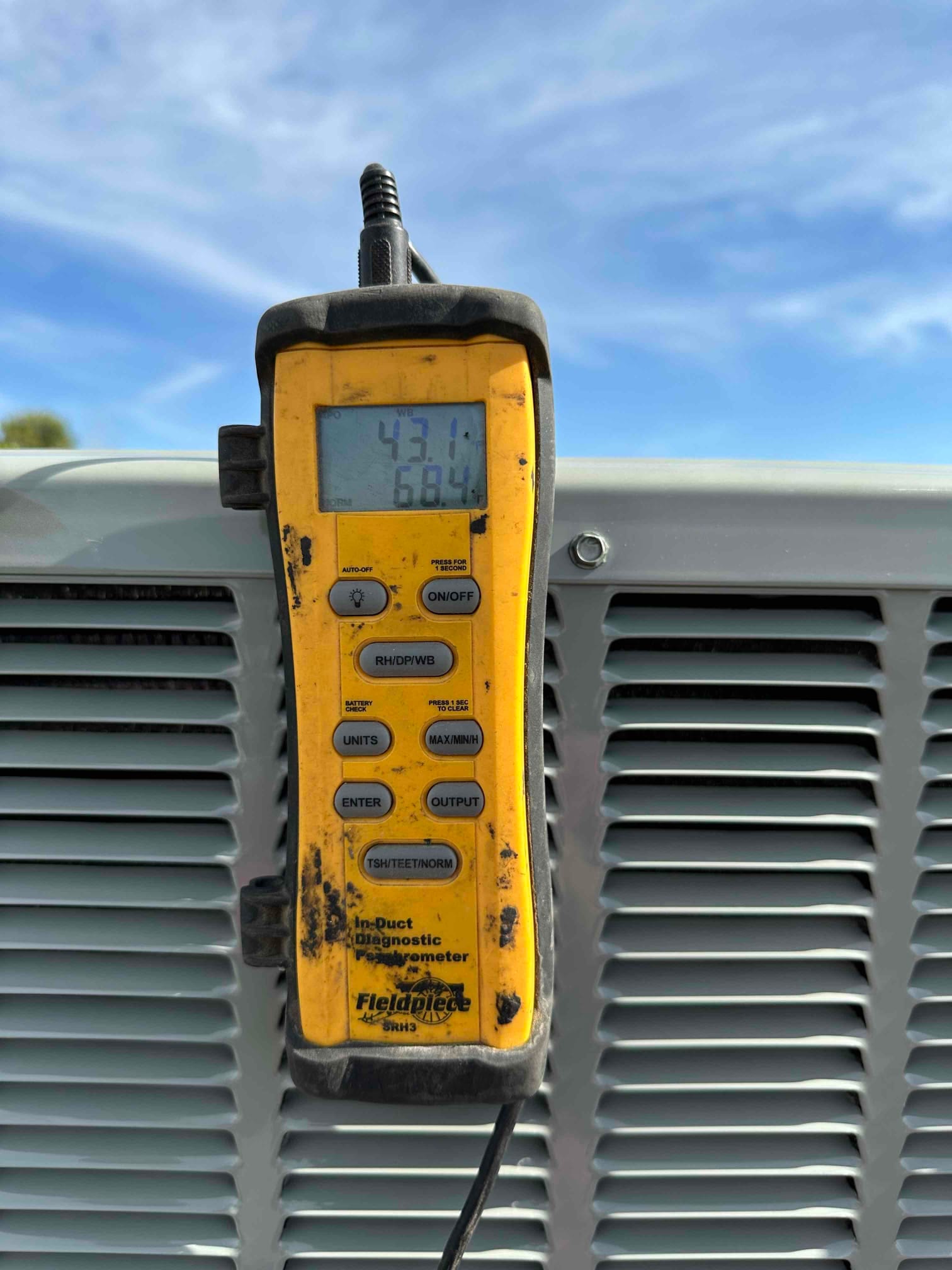 Digital psychrometer displays 68.4°F while measuring air conditions at the outdoor unit during commissioning.