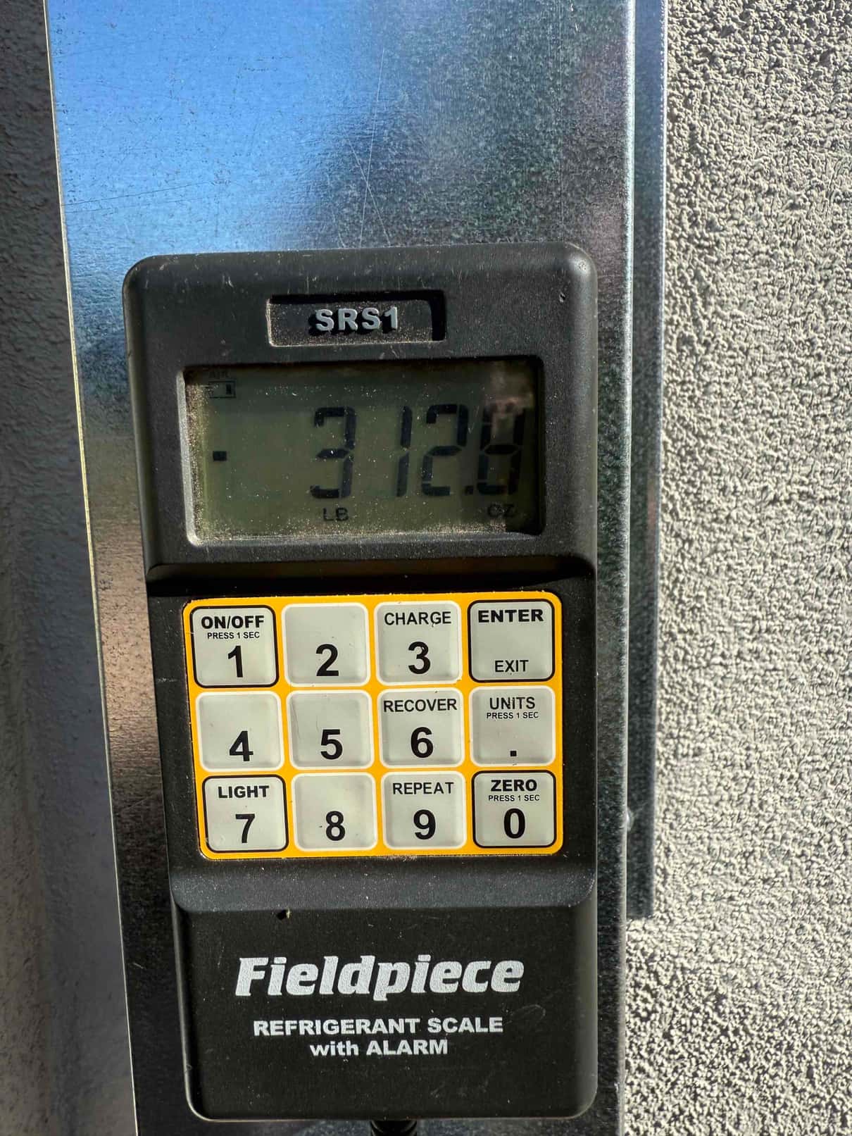 Digital refrigerant scale display shows 31.28 pounds during charging process, with control keypad and functions visible.
