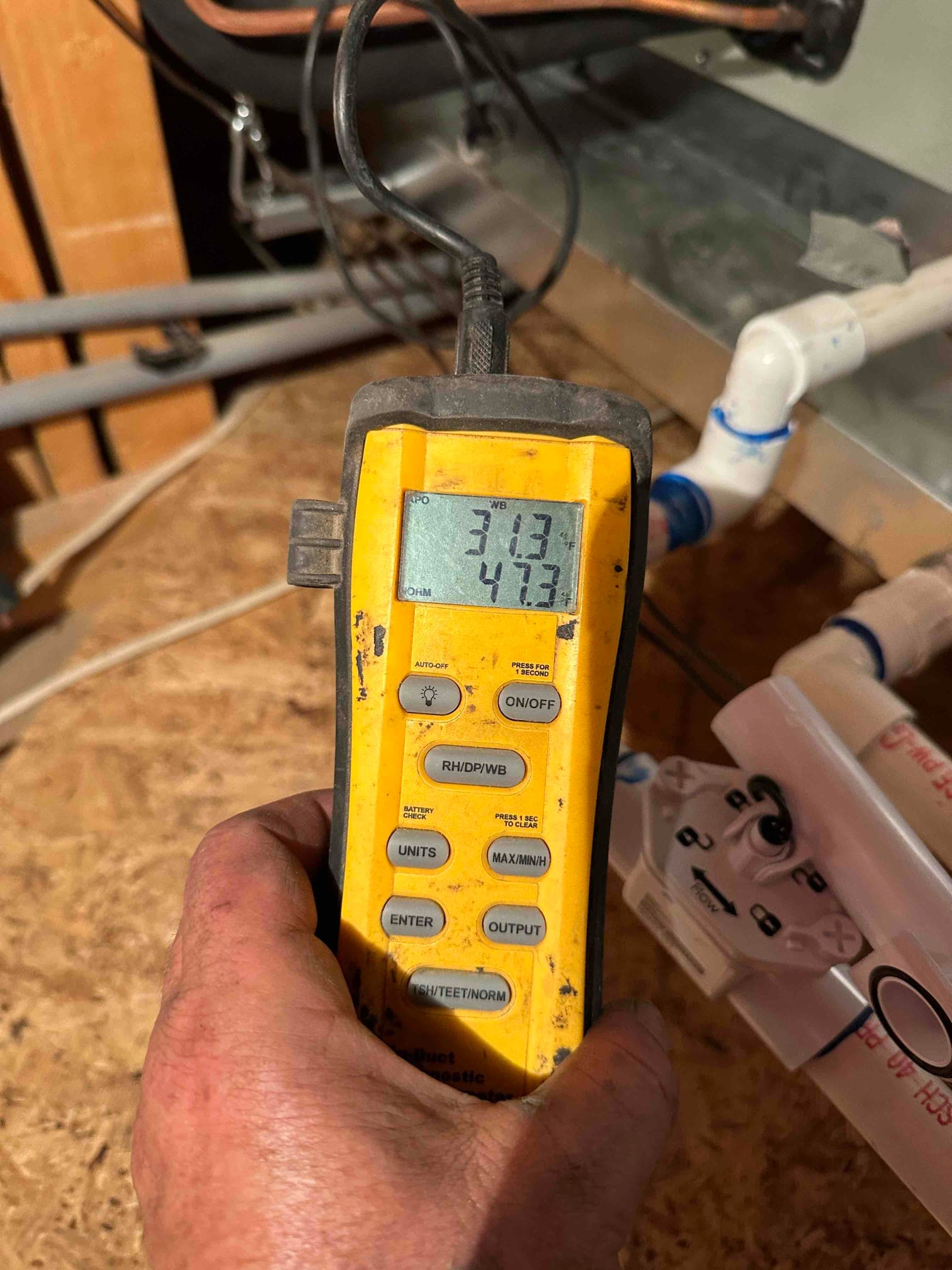 Digital thermometer at the air handler shows temperatures of 31.3 and 47.3 degrees during airflow commissioning.