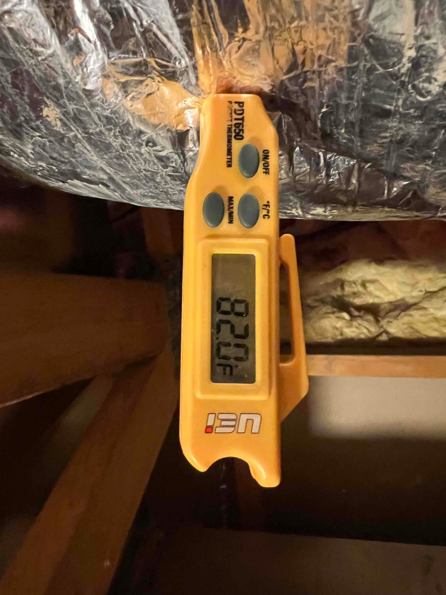 Digital thermometer clipped to insulated duct shows 82.0°F, documenting return air temperature during commissioning.