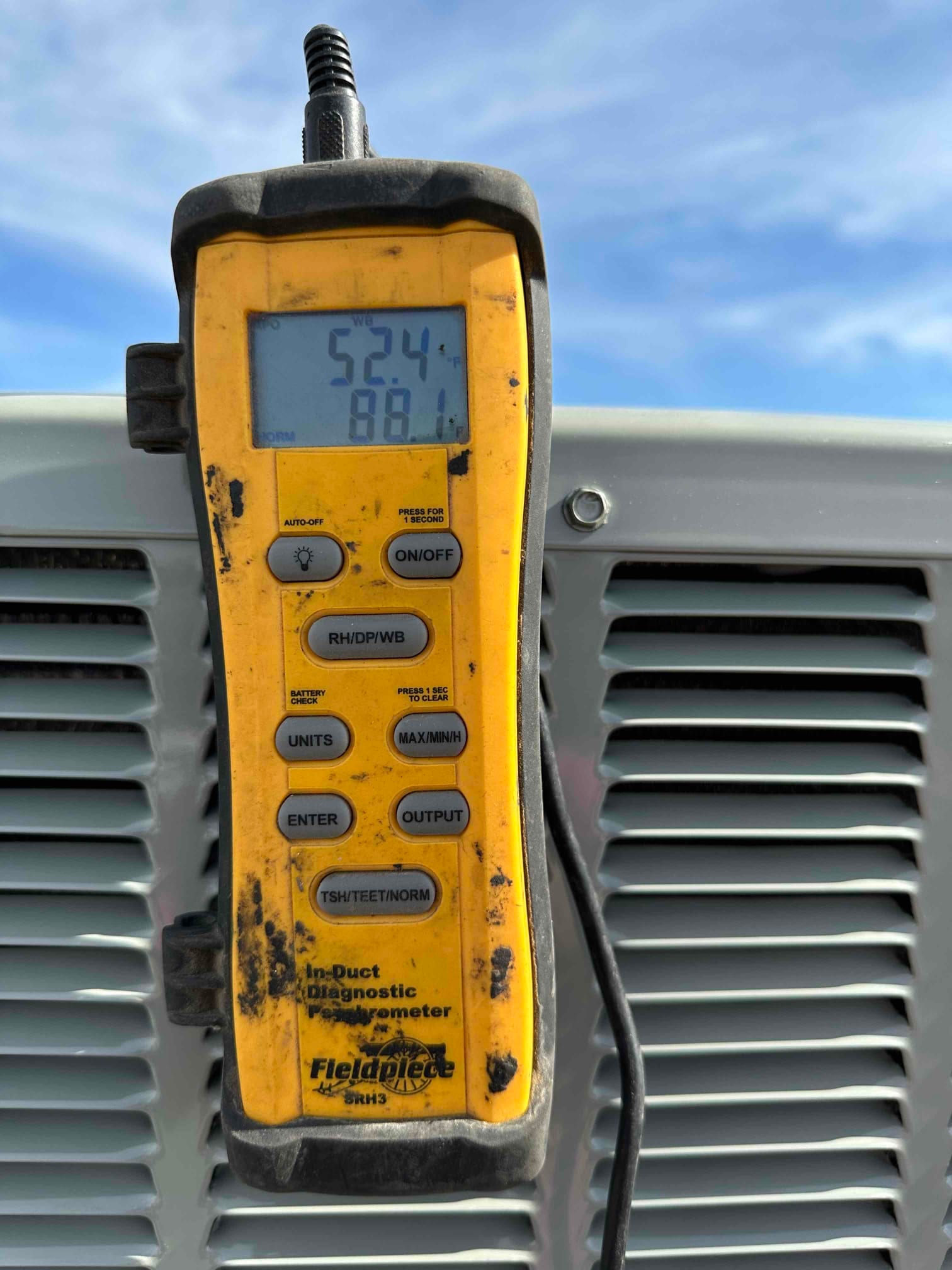 Digital thermometer displays 52.4 degrees Fahrenheit while measuring air temperature during system commissioning at the outdoor unit.