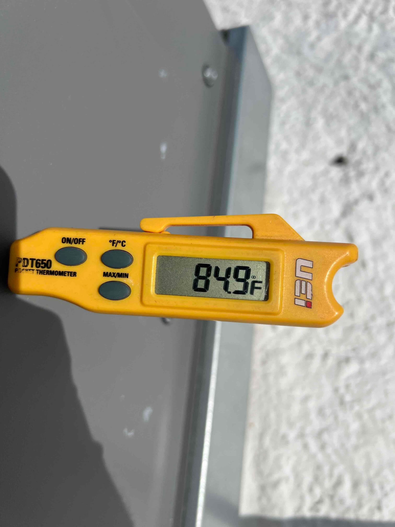 Digital thermometer displays 84.9 degrees Fahrenheit while measuring air temperature during system commissioning.