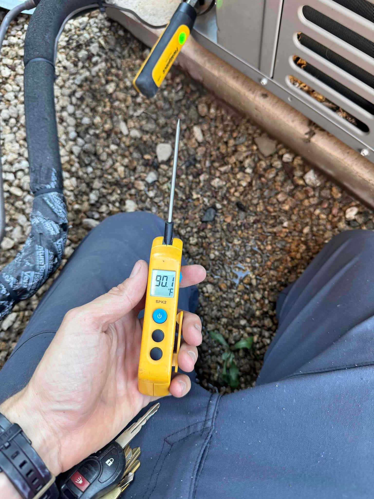 Digital thermometer displays 90.7 °F with the probe inserted near the HVAC unit during service.