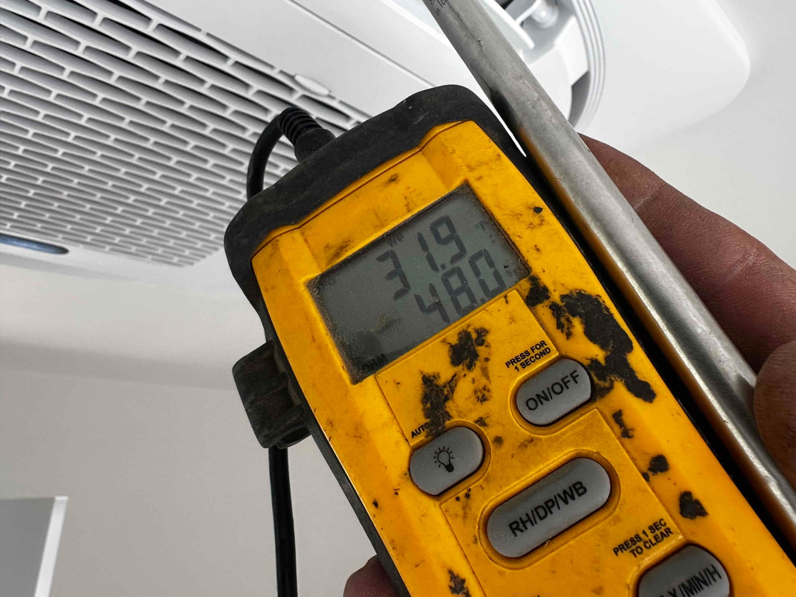 Digital thermometer held at a mini‑split indoor unit grille shows 48 degrees Fahrenheit during supply air temperature check.