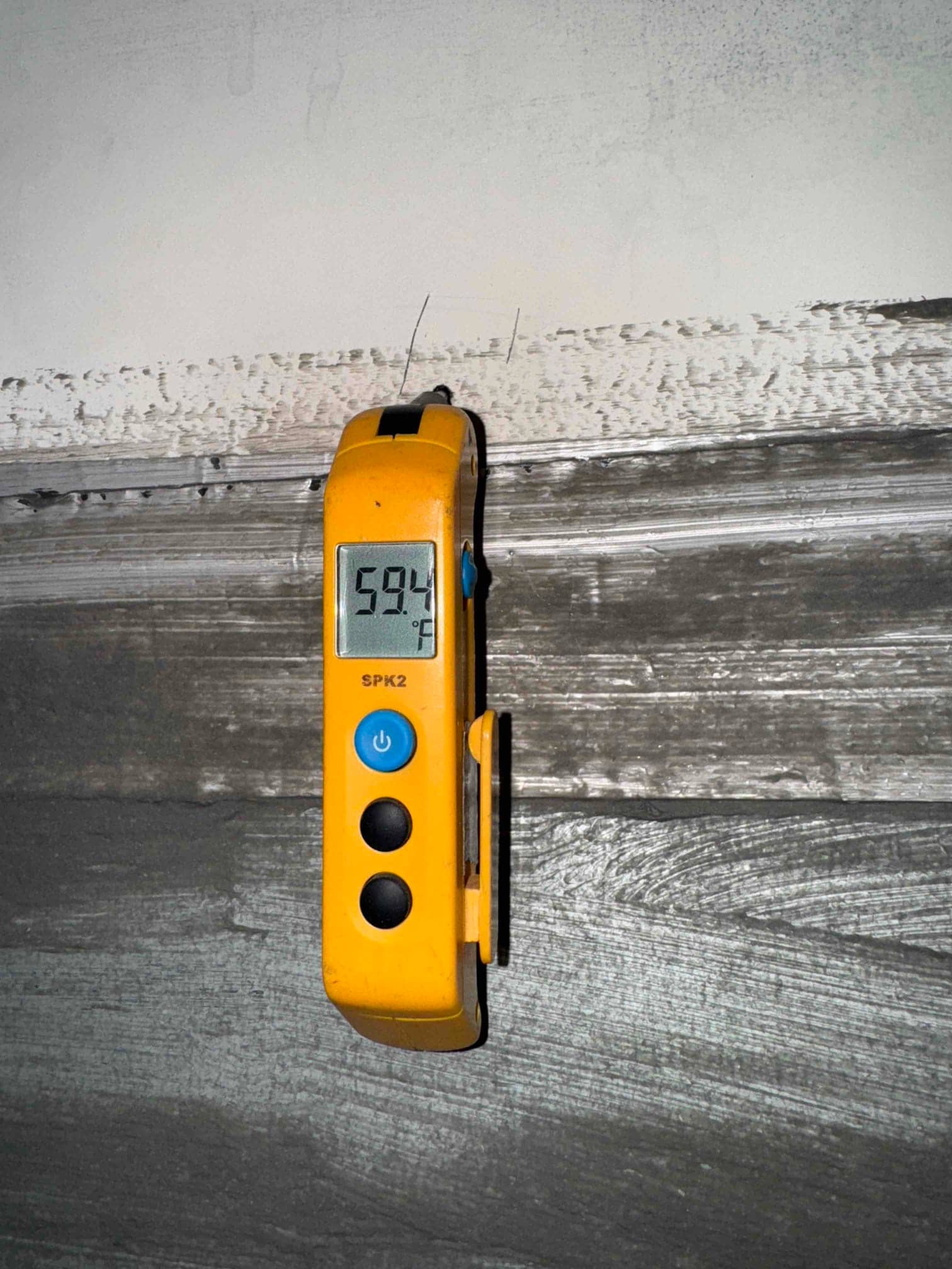 Digital thermometer shows 59.4 °F while measuring the wall surface near the condensate drain area.