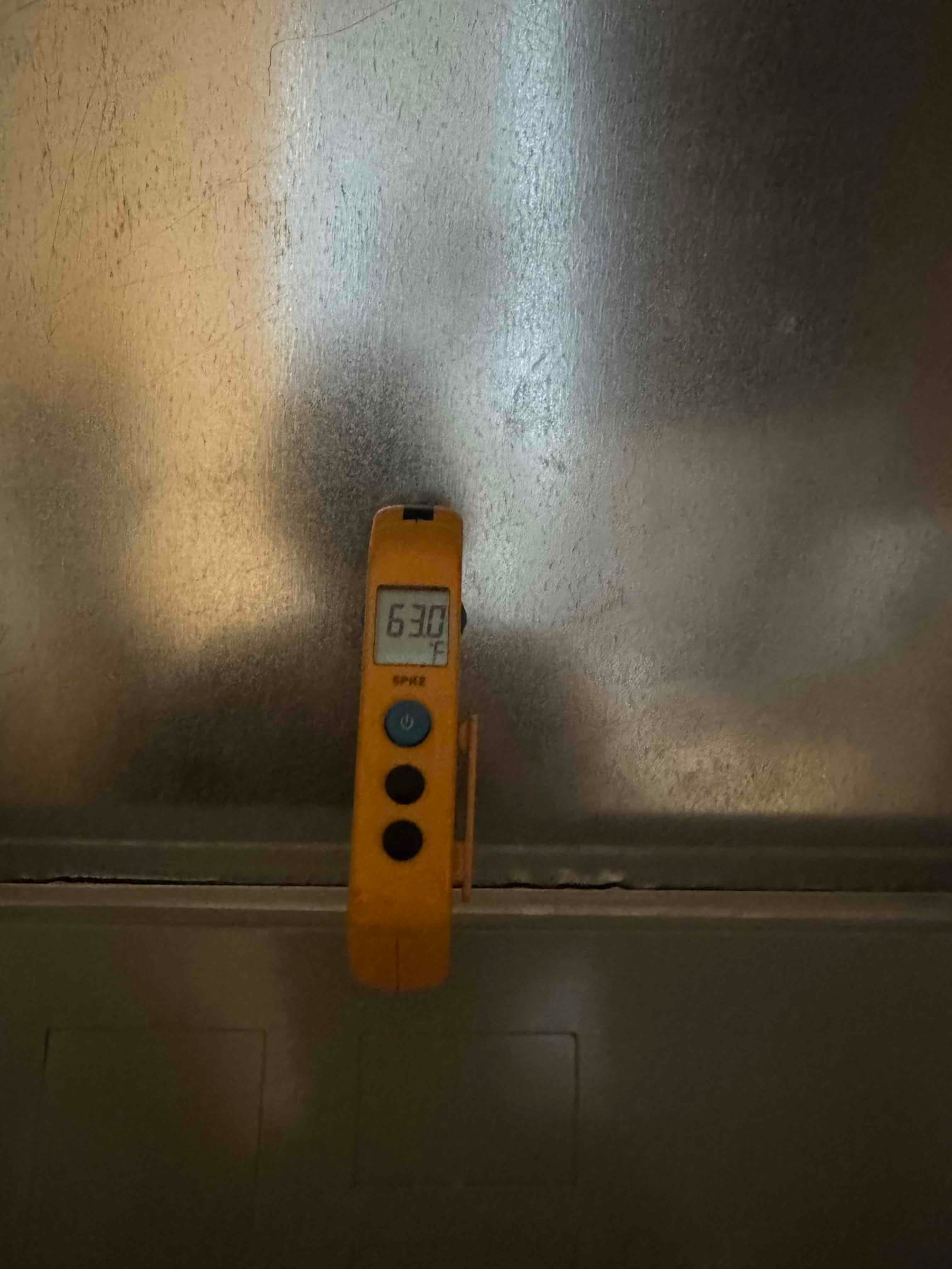Digital thermometer shows 63.0 °F on the air handler cabinet during condensate drain line repair and flush.
