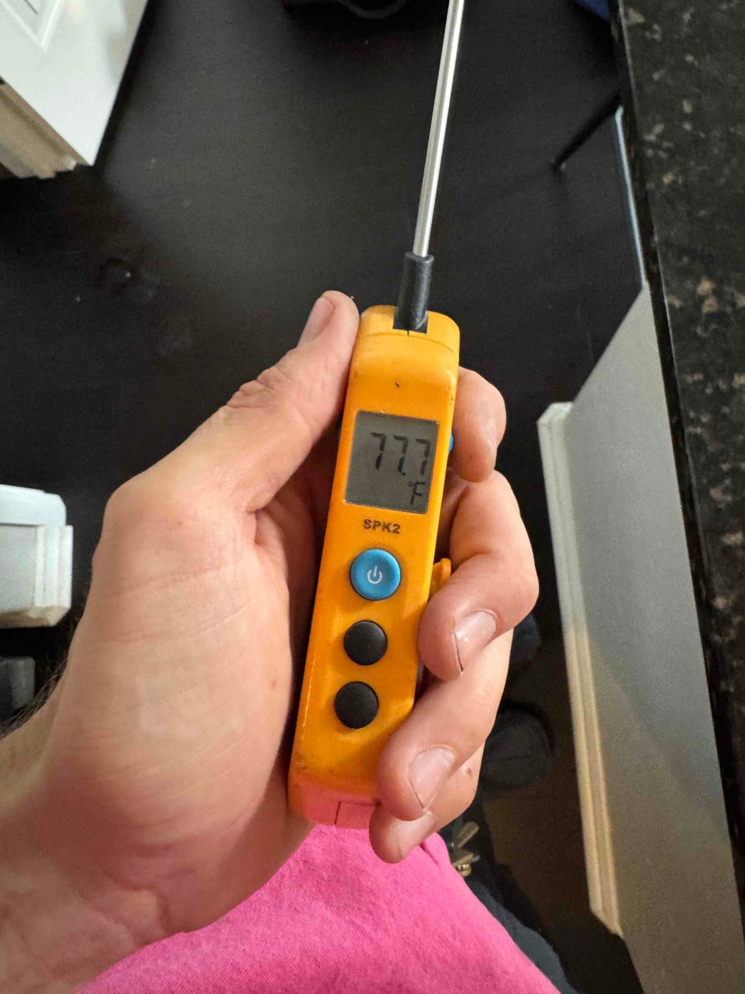 Digital thermometer shows 77.7 °F on the probe while checking temperature during condensate drain line maintenance.