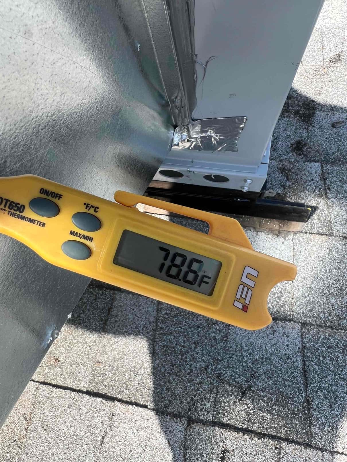 Digital thermometer shows 78.6°F while measuring air temperature at the duct connection on the rooftop unit.