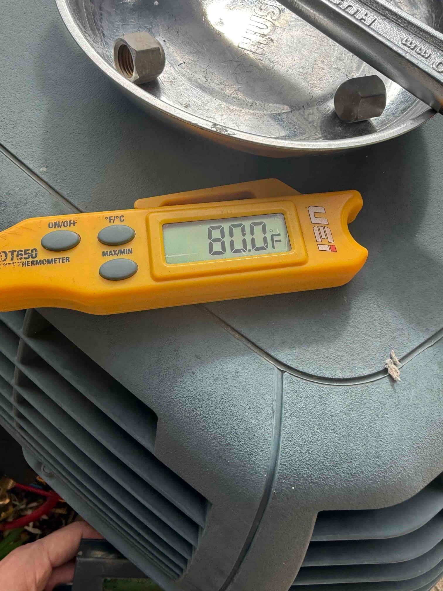 Digital thermometer shows 80.0 °F while measuring temperature on the outdoor condenser housing during refrigerant recharge work.