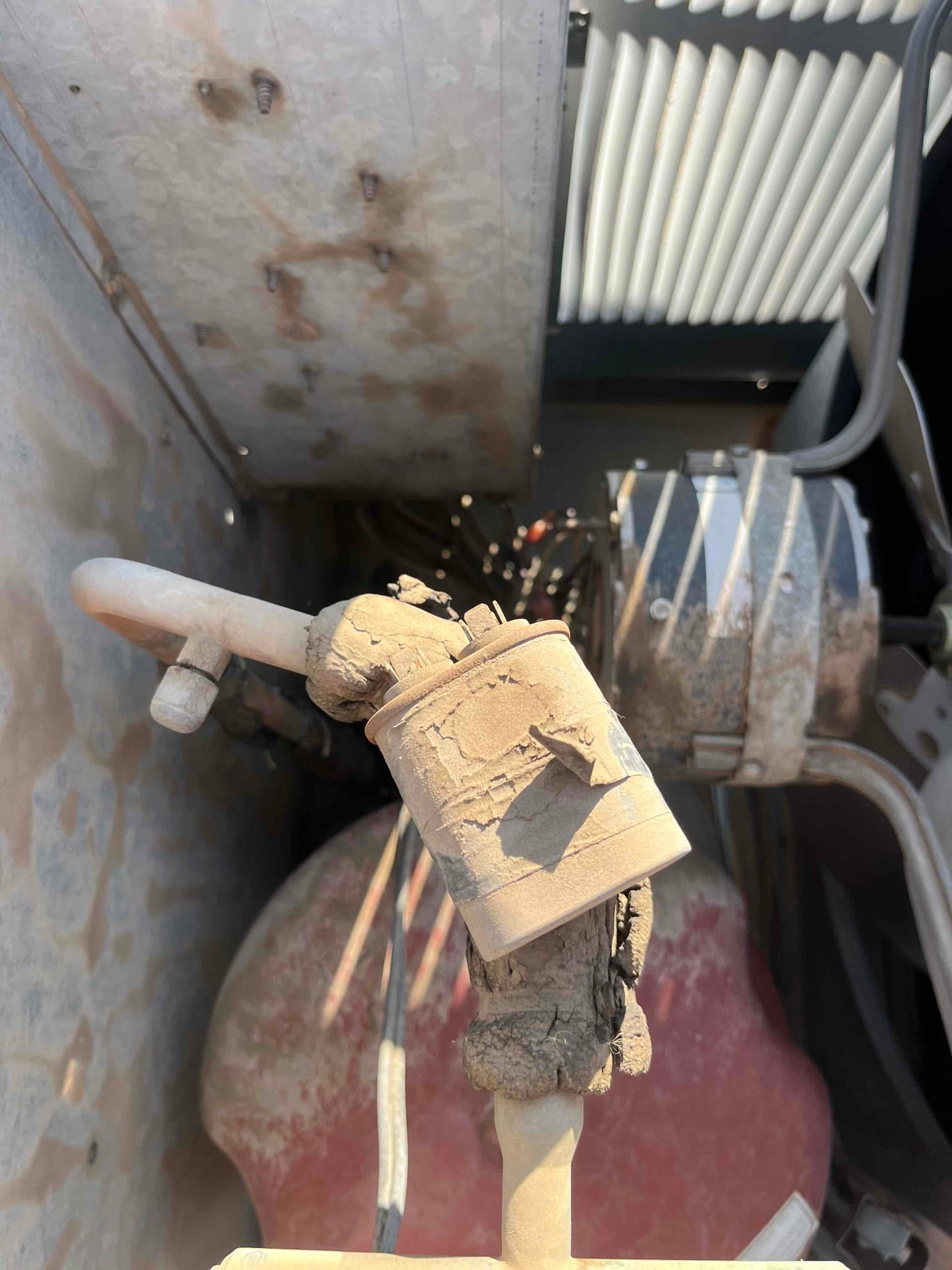 Dust-covered condenser fan motor area with a heavily corroded and dirty capacitor canister mounted on the refrigerant line.