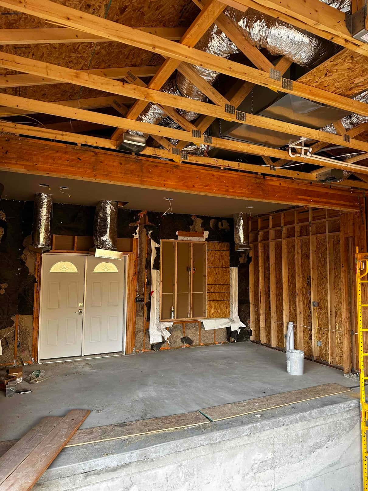 Exposed framing with newly run insulated flex ducts and a suspended metal plenum installed in the ceiling of a renovation space.