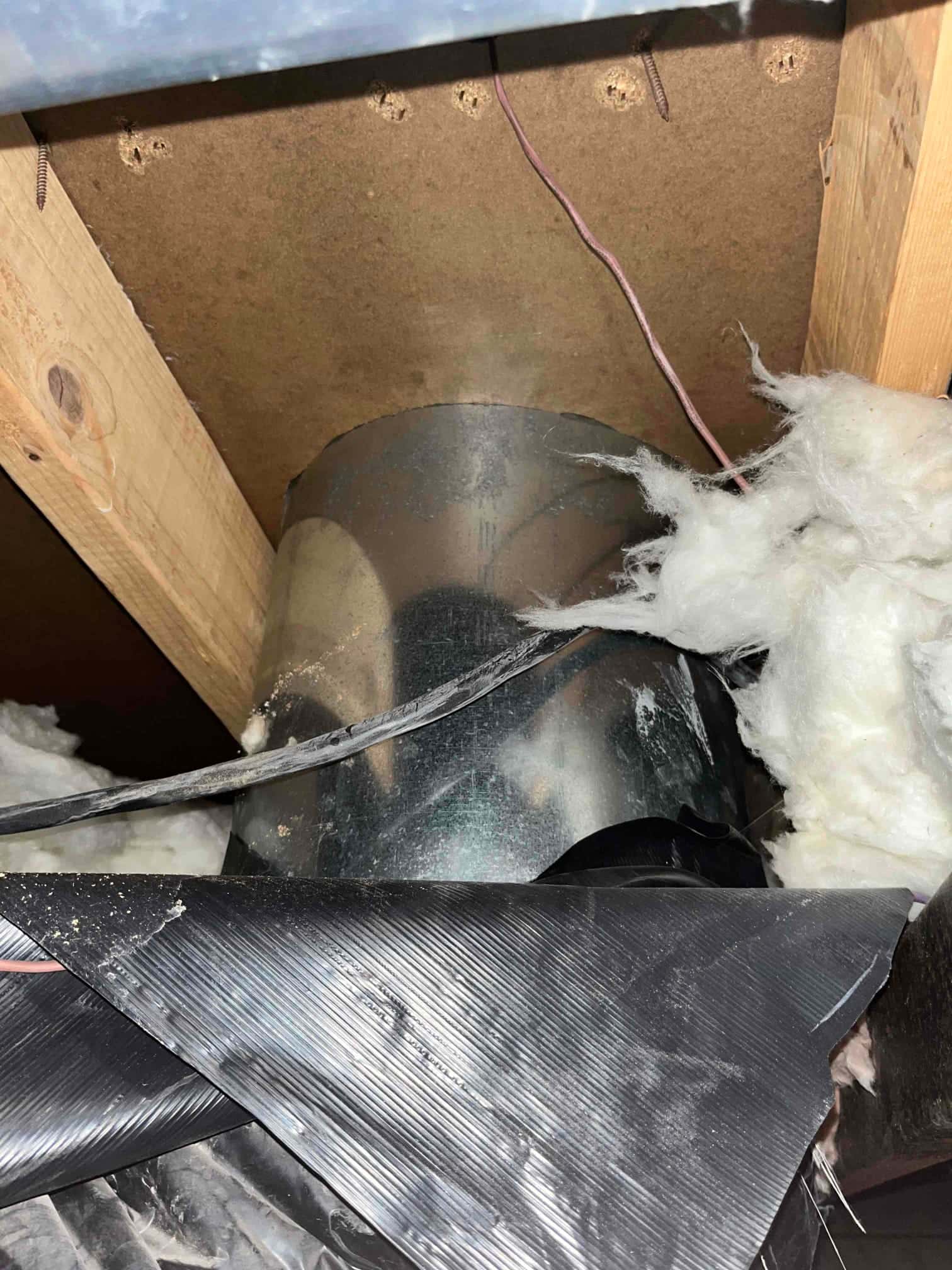 Flexible duct and insulation pulled back, exposing a metal round duct section between framing members in the attic.