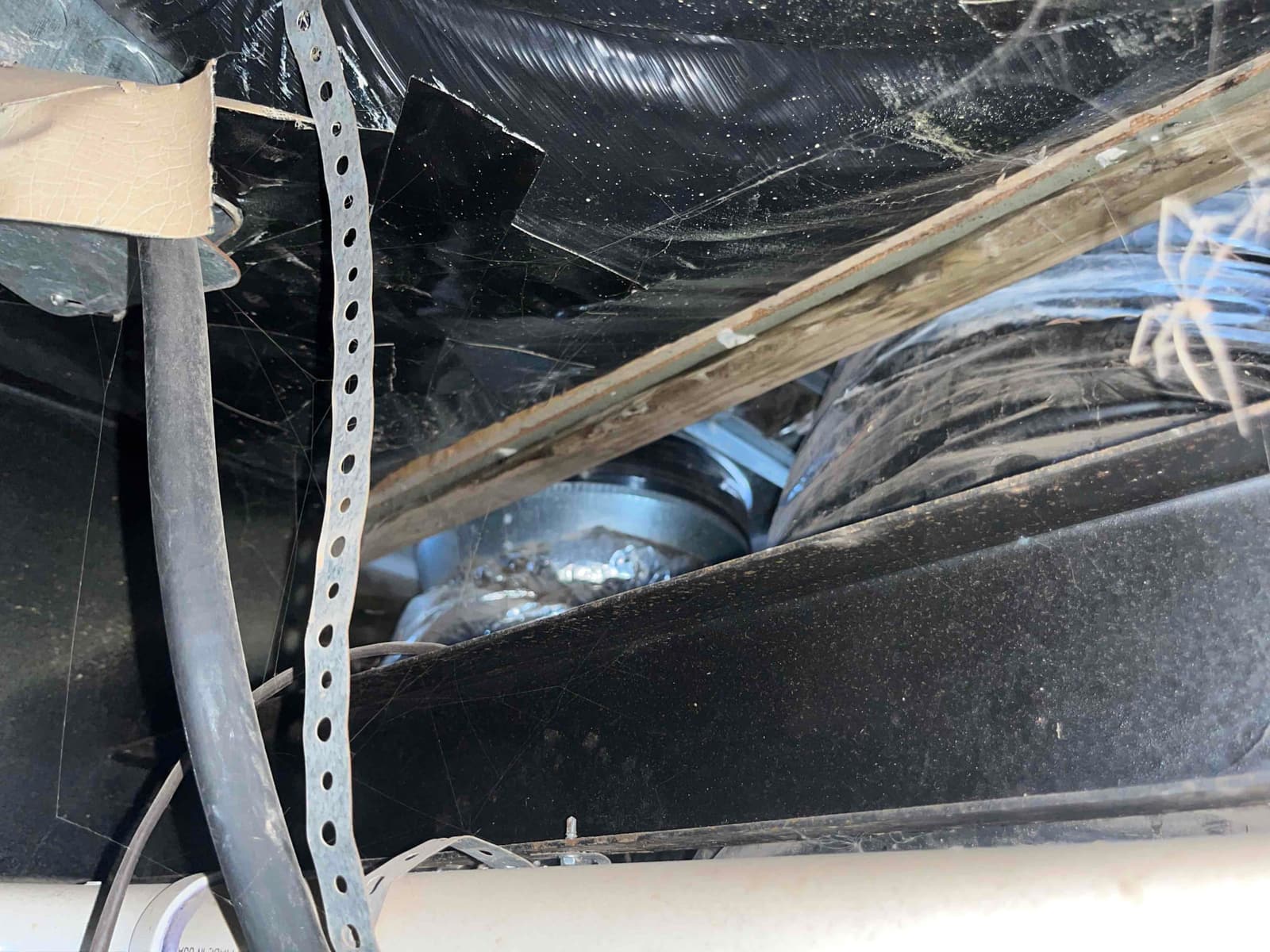 Flexible duct and metal duct connection in an attic space, showing tape-sealed joint, support strap, and surrounding dust.