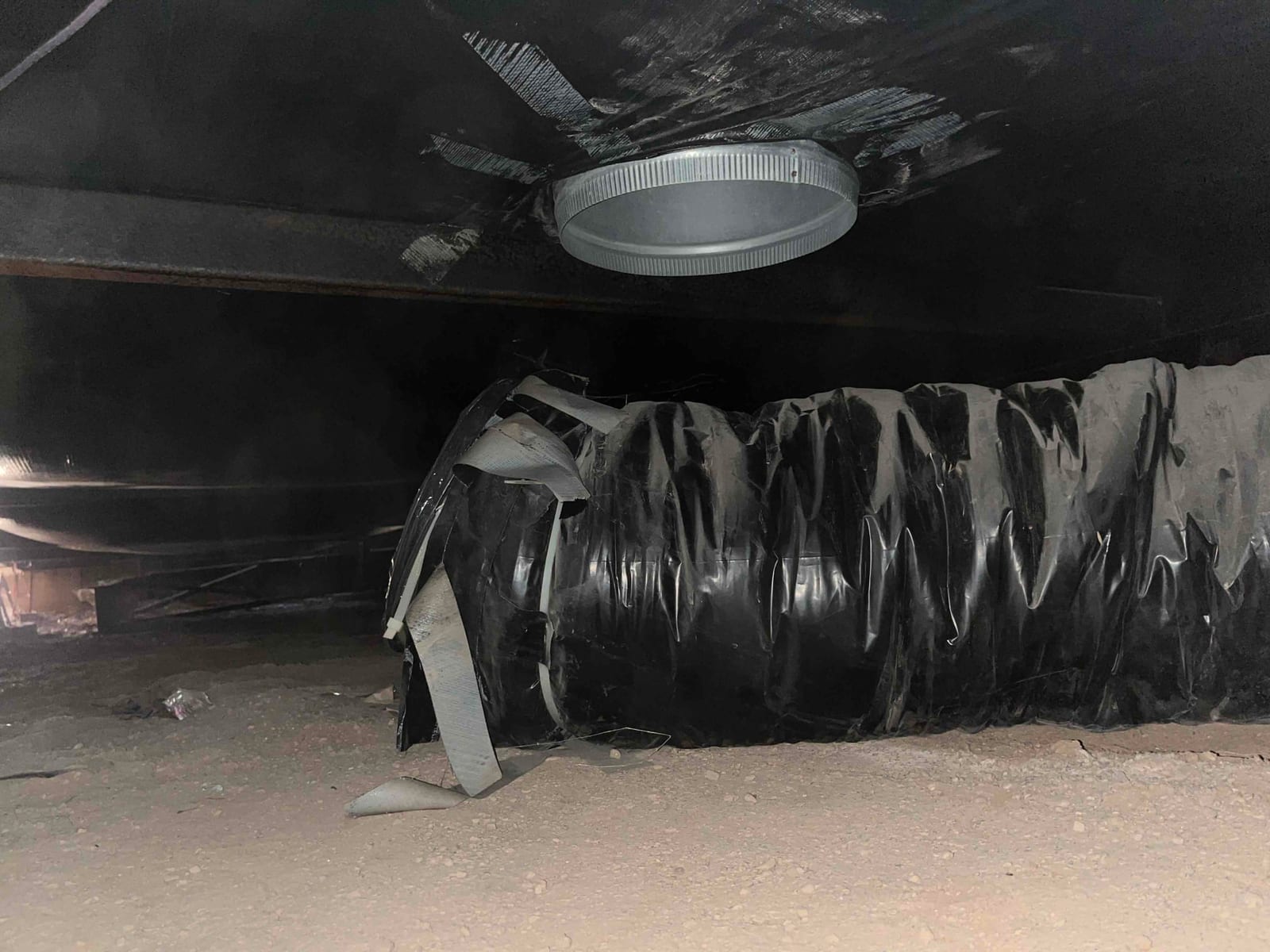 Flexible insulated duct in a crawlspace is torn and detached near a round metal takeoff collar, exposing inner liner.