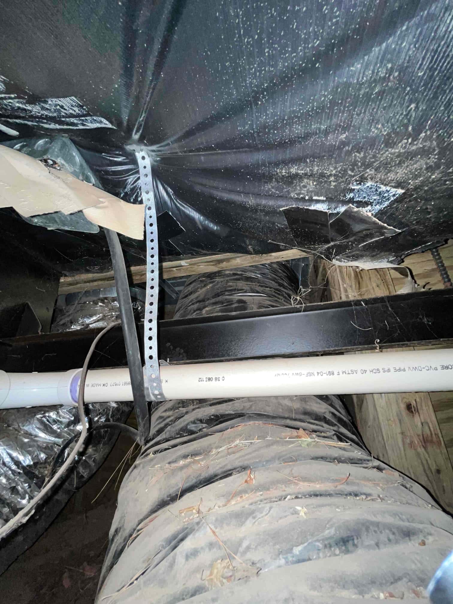 Flexible insulated duct and PVC condensate drain line run through a crawlspace, secured with strap and supported by framing.