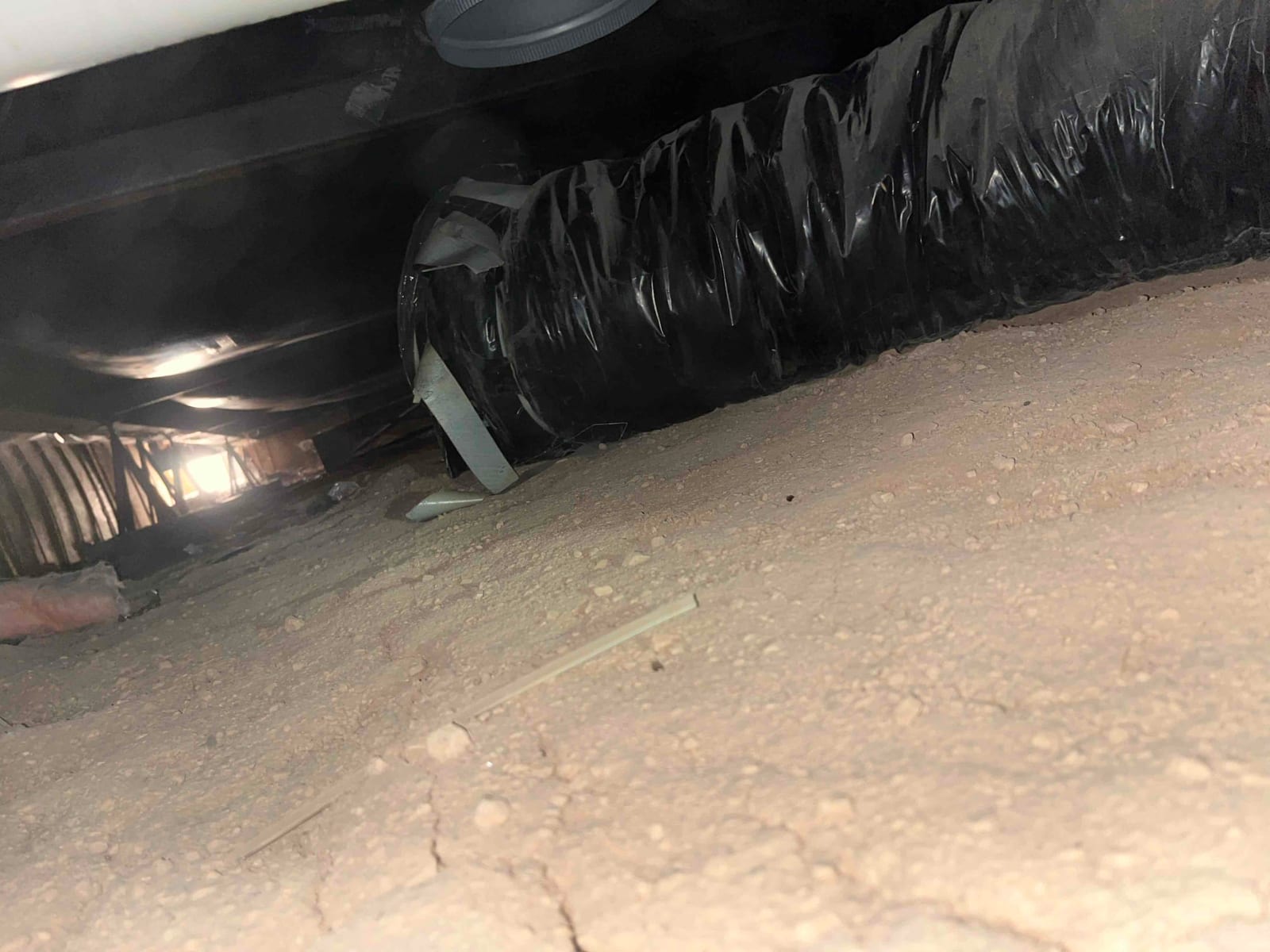 Flexible insulated duct run in a crawlspace, with tape-secured joint and surrounding bare soil floor visible.