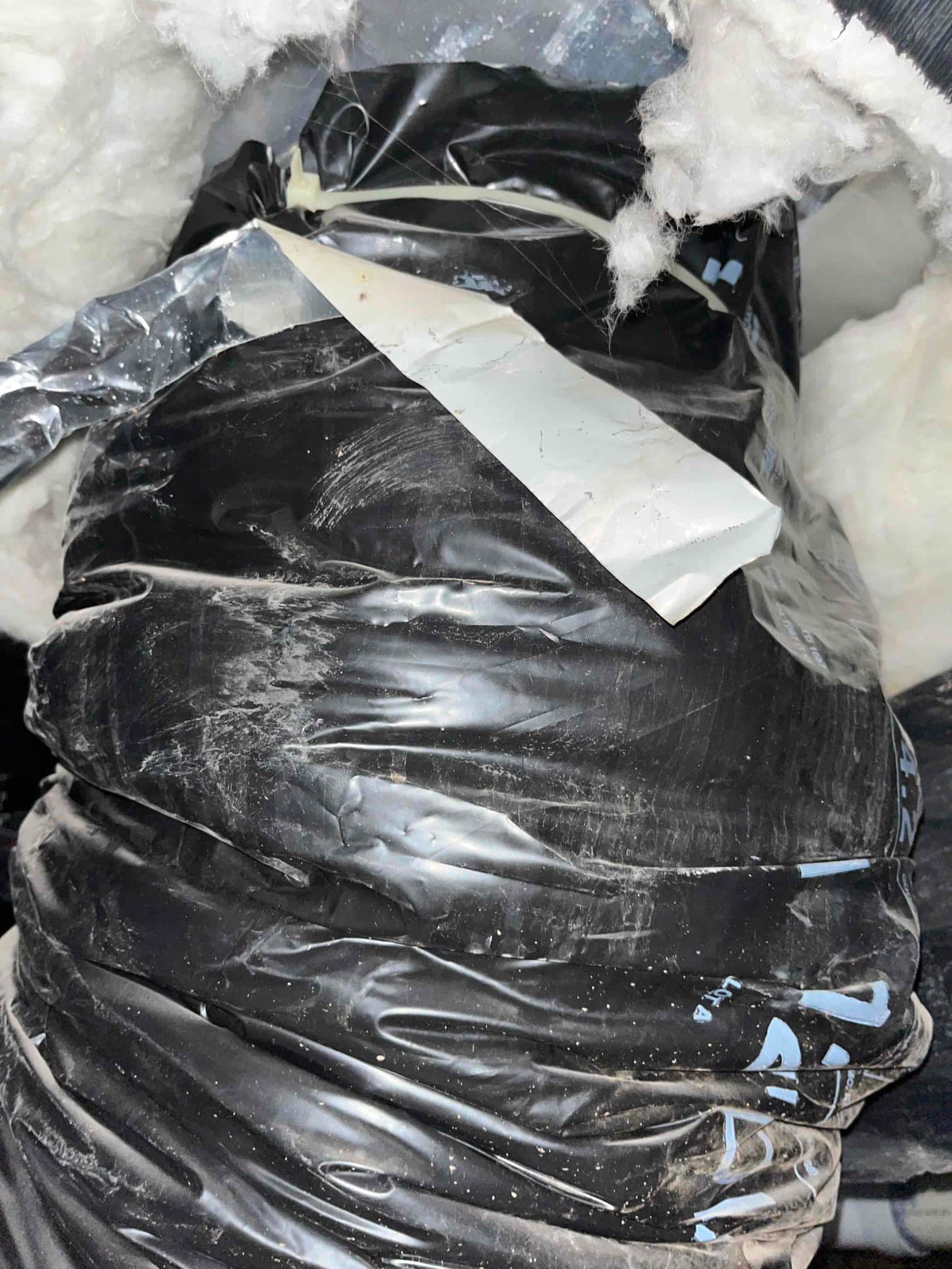 Flexible insulated duct with torn outer jacket and exposed fiberglass insulation near a taped seam.