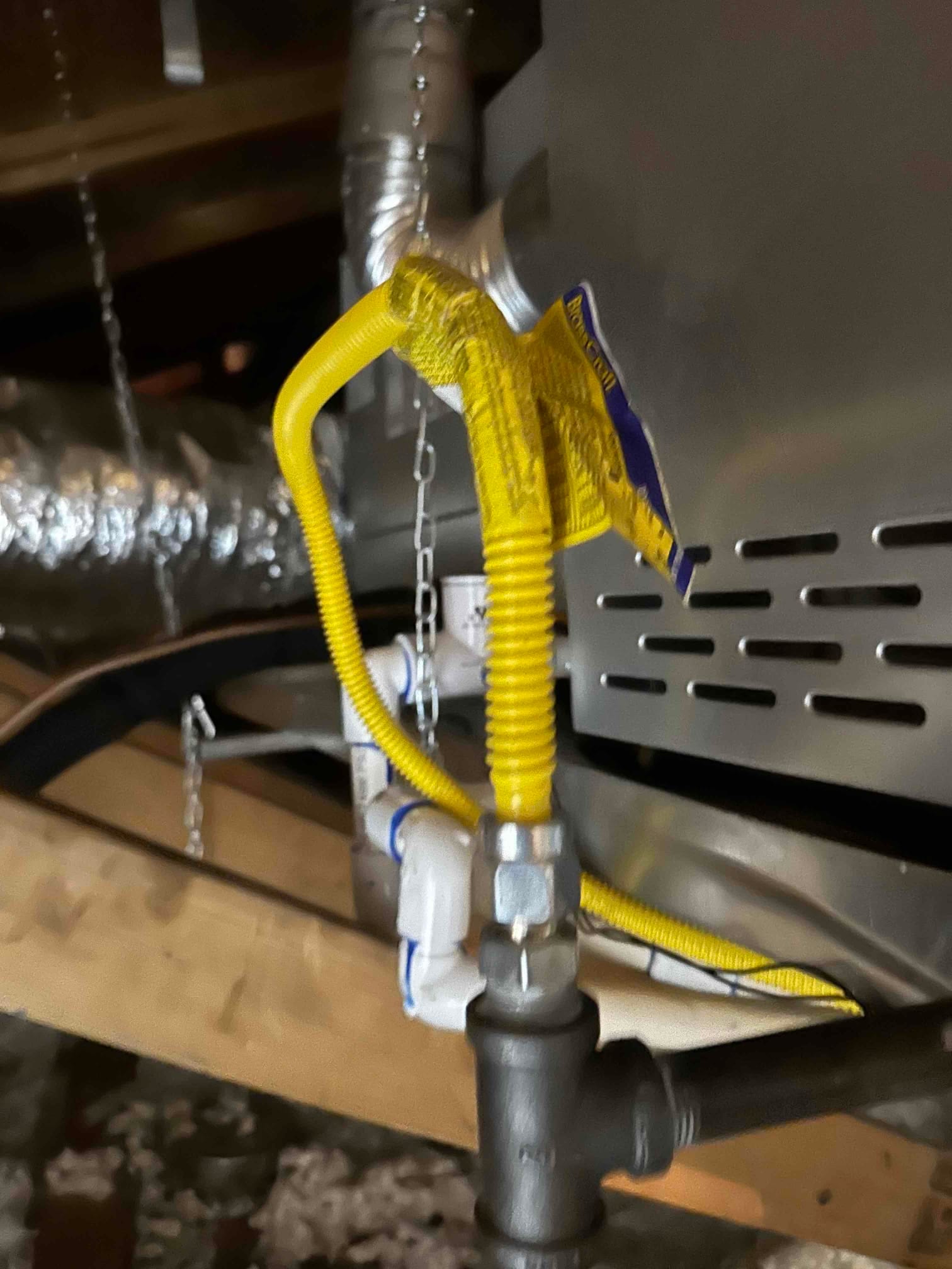 Flexible yellow gas connector ties into the black iron gas line at the furnace in the attic installation.