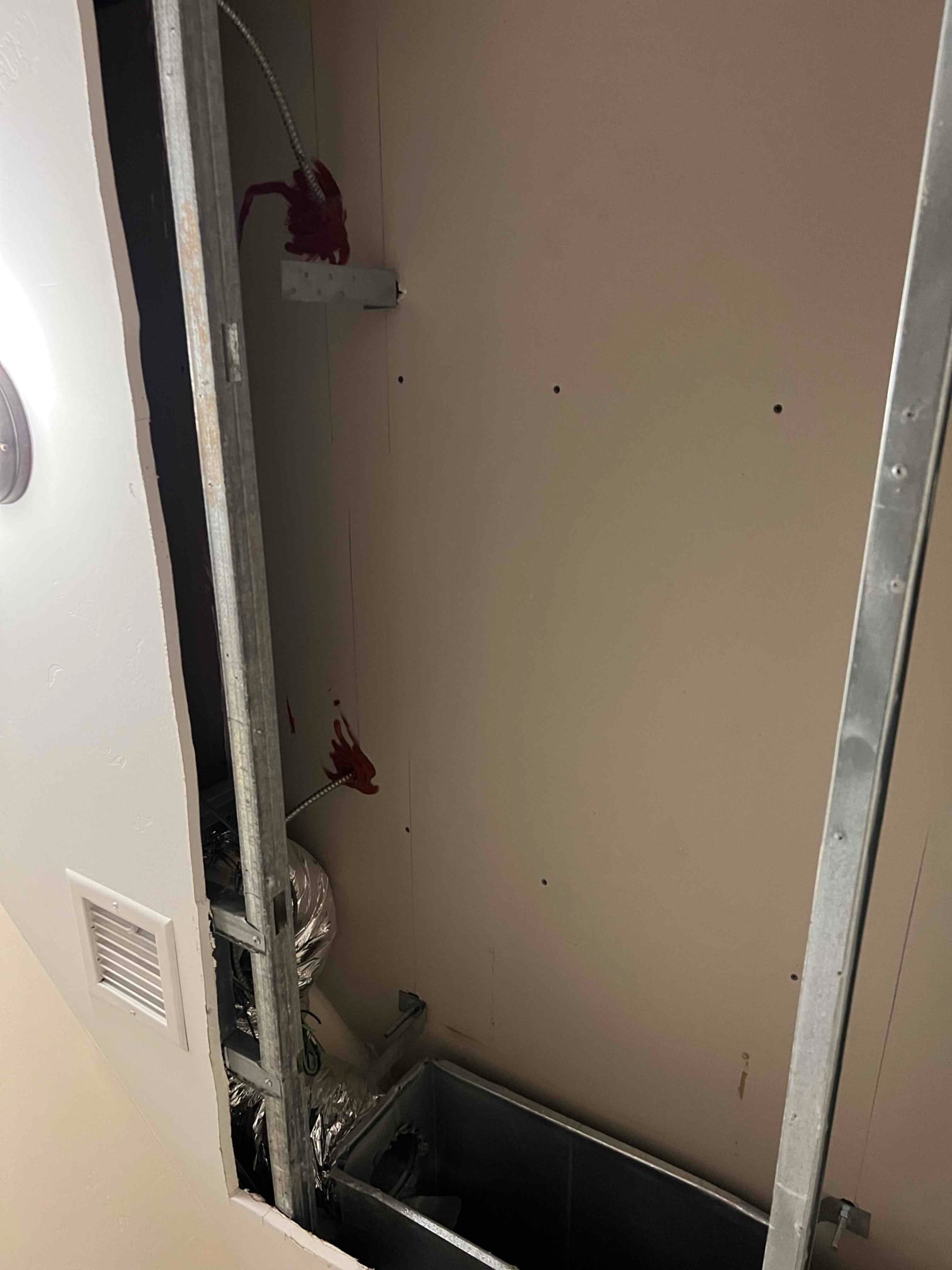 Framed wall opening exposes ductwork and flexible insulated duct with electrical whip during air handler installation preparation.