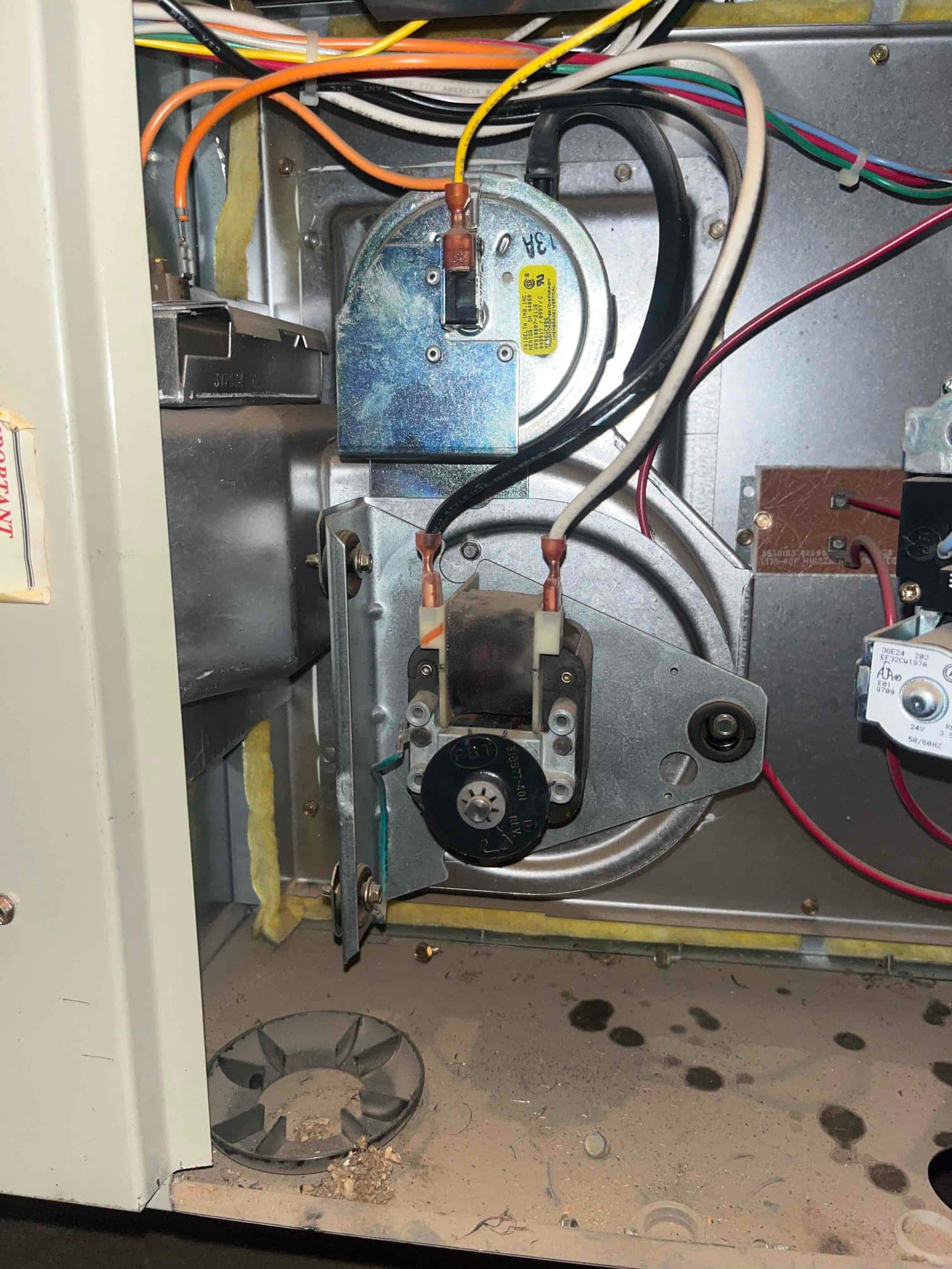 Furnace inducer draft assembly and blower wheel visible inside open cabinet, with wiring connected and dust present on the cabinet floor.