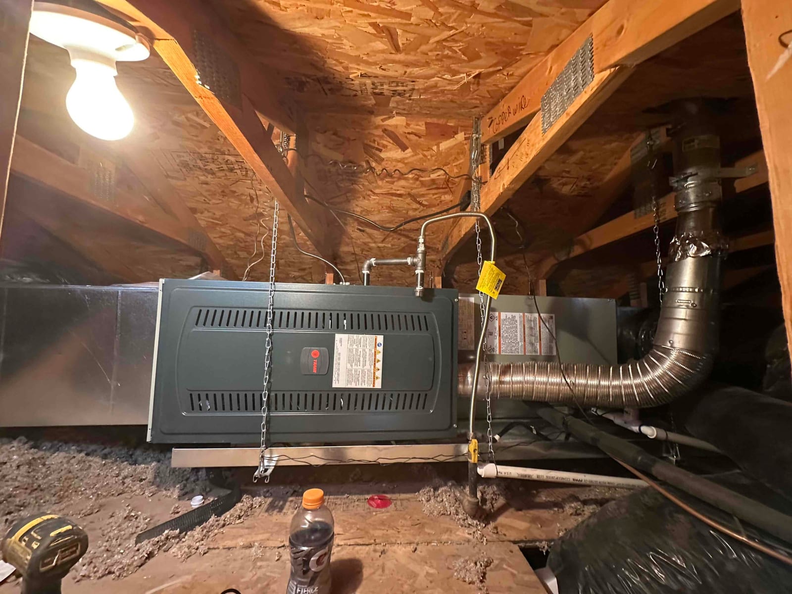Gas furnace hung from attic rafters with new metal duct connections, vent flue, and gas piping secured and labeled.