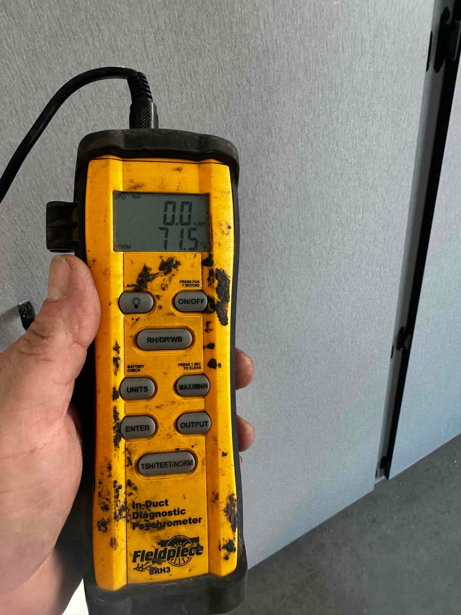 Handheld digital thermometer displays 71.5 degrees Fahrenheit during air temperature check near the indoor unit.