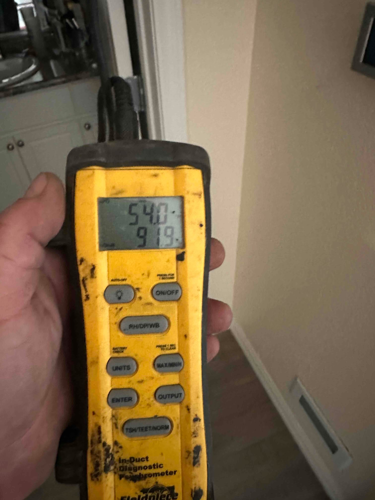 Handheld digital thermometer shows 54.0 degrees Fahrenheit while measuring supply air at a floor register during commissioning.