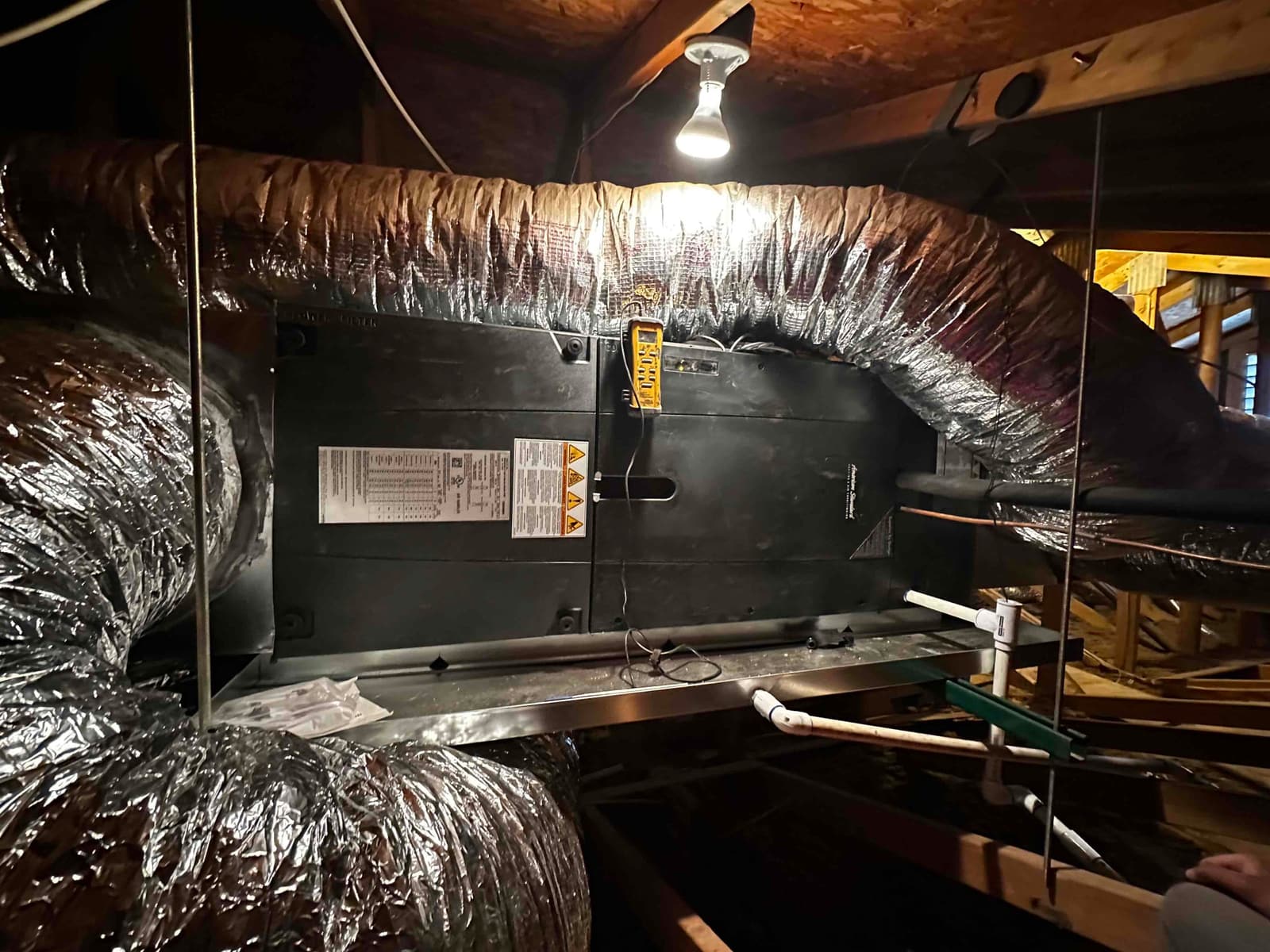 Horizontal air handler installed in attic with insulated duct connections and PVC condensate drain piping on a suspended secondary drain pan.