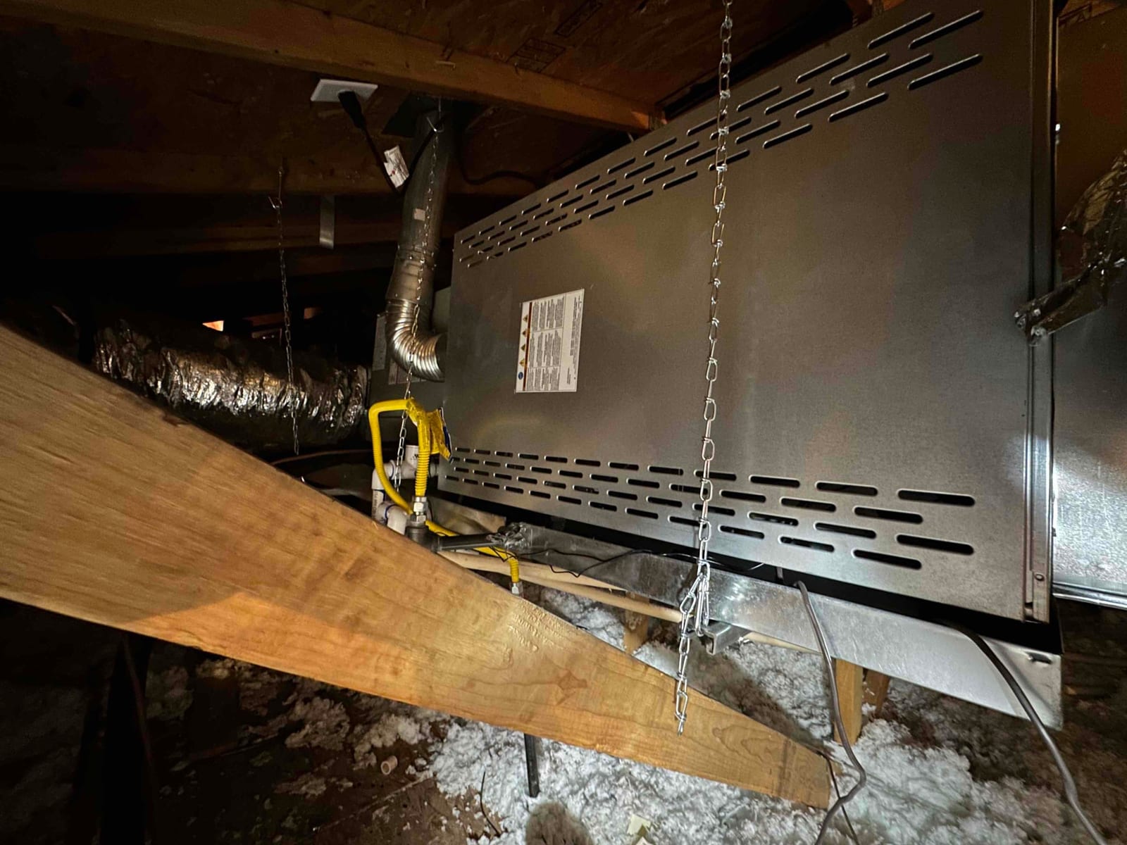 Horizontal air handler suspended in an attic with flex duct connections, gas line, and drain pan visible beneath.