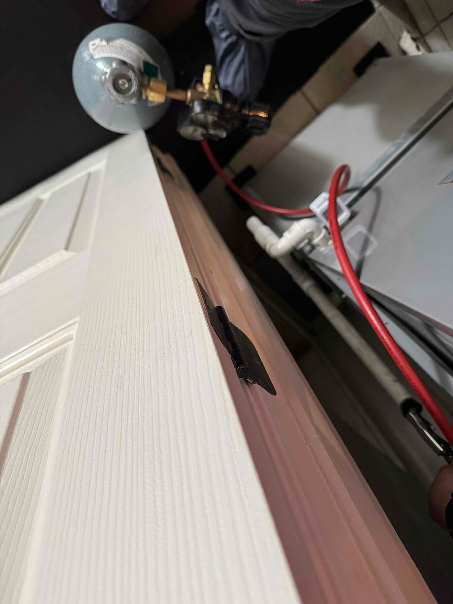 HVAC technician services an indoor air handler; red hose connects to equipment and white PVC condensate drain line is visible.